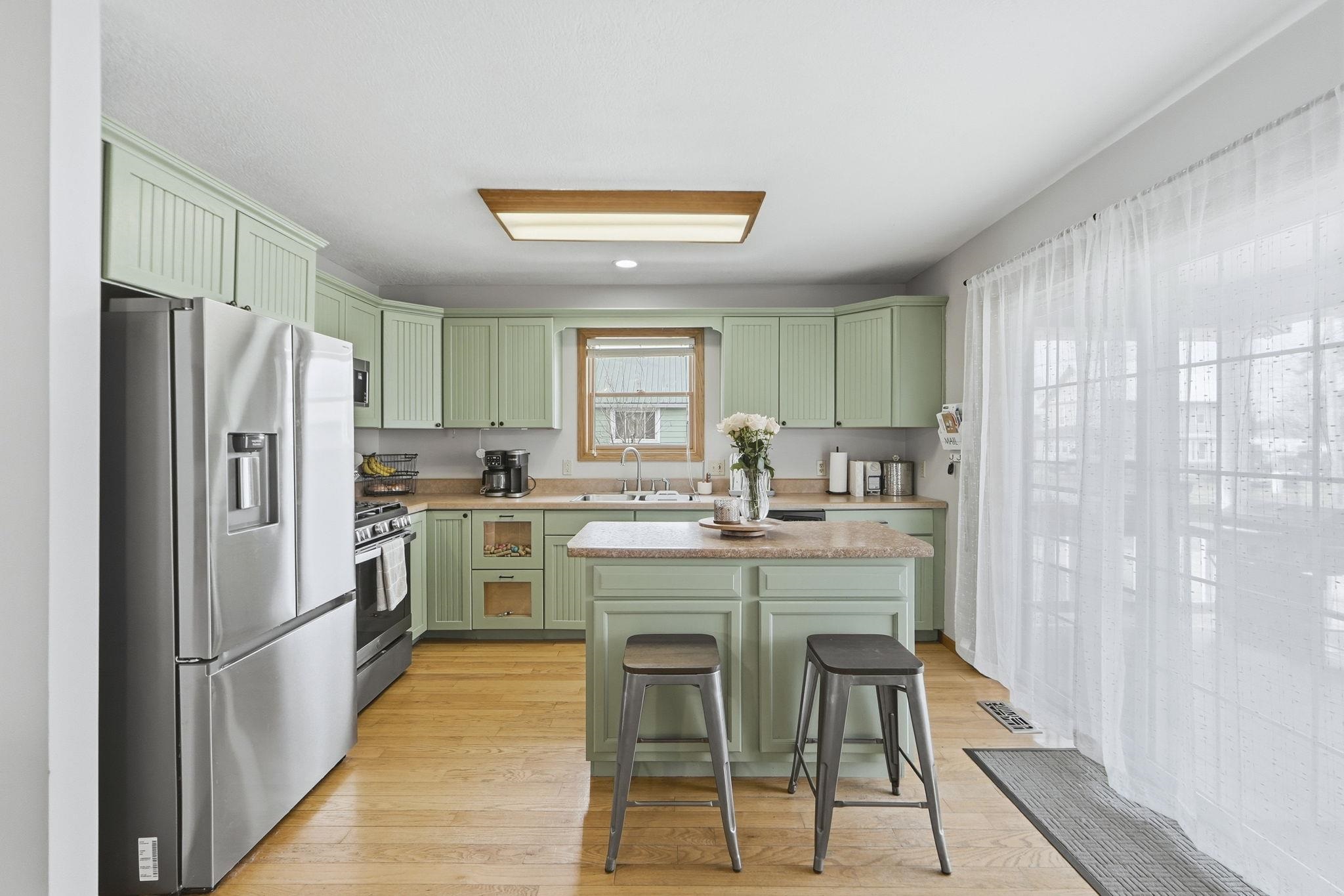 Kitchen featuring green cabinetry, stainless steel appliances, light countertops, light wood-style flooring, and a kitchen breakfast bar