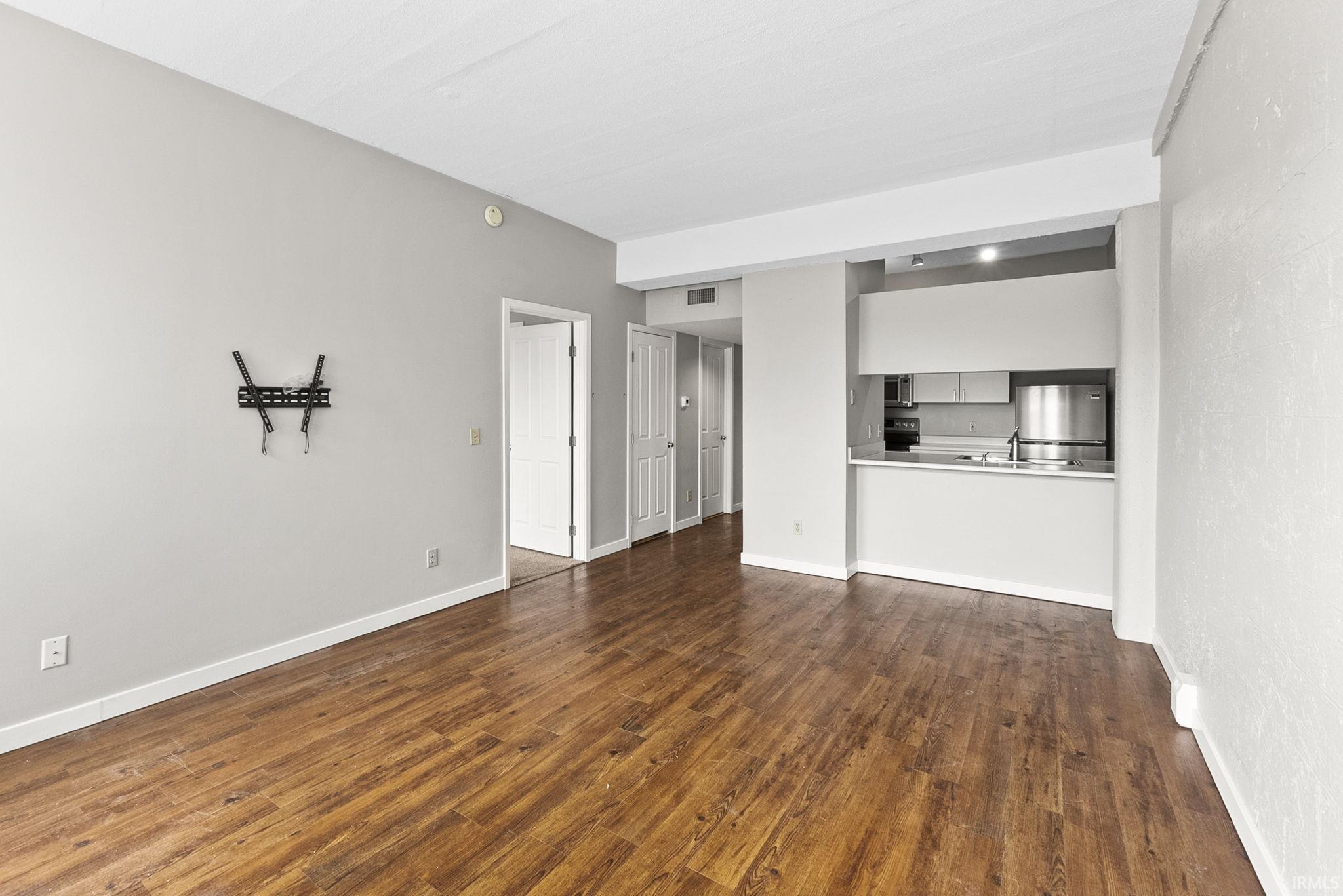Unfurnished living room featuring dark wood finished floors and baseboards