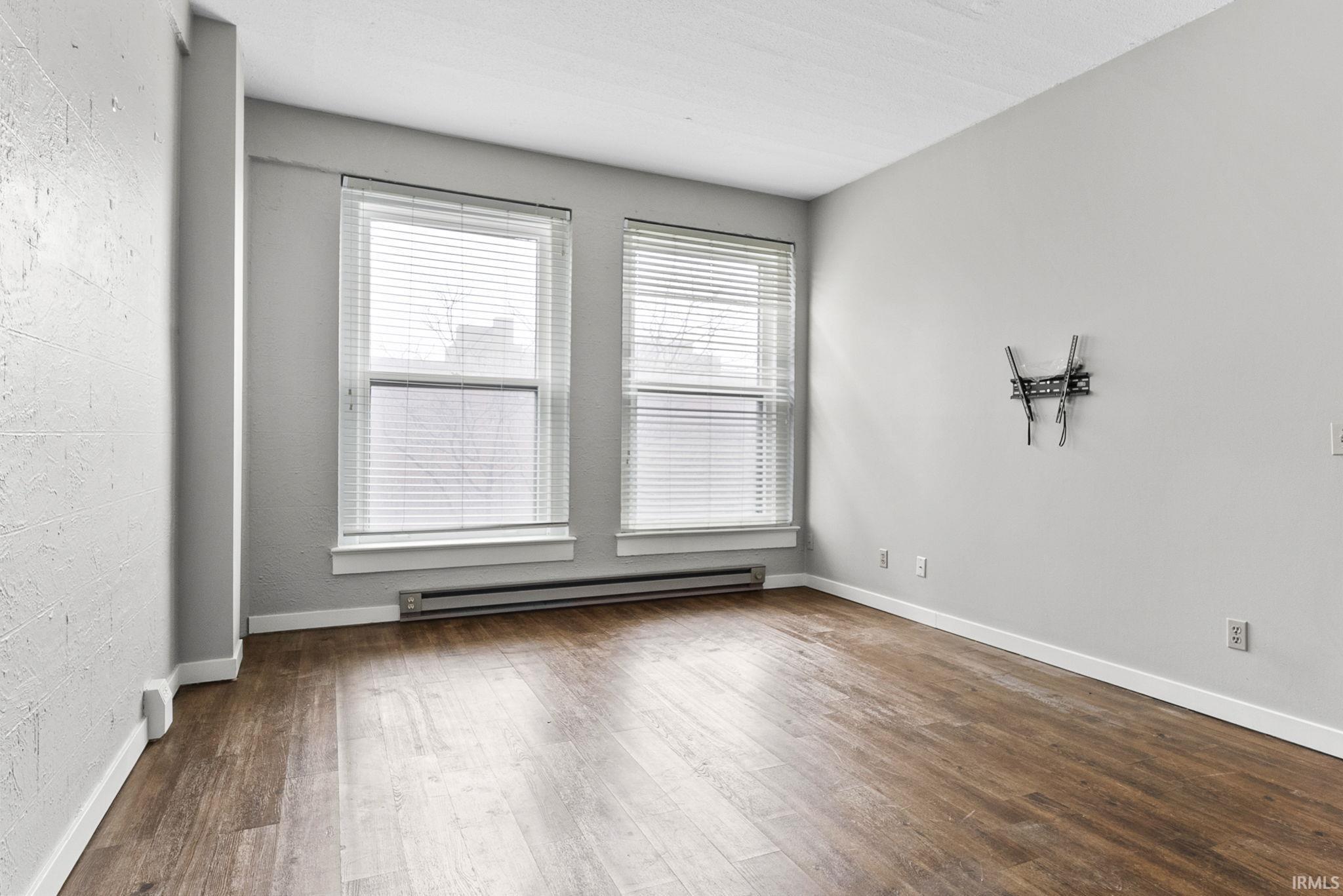 Unfurnished room with baseboard heating and dark wood-style flooring