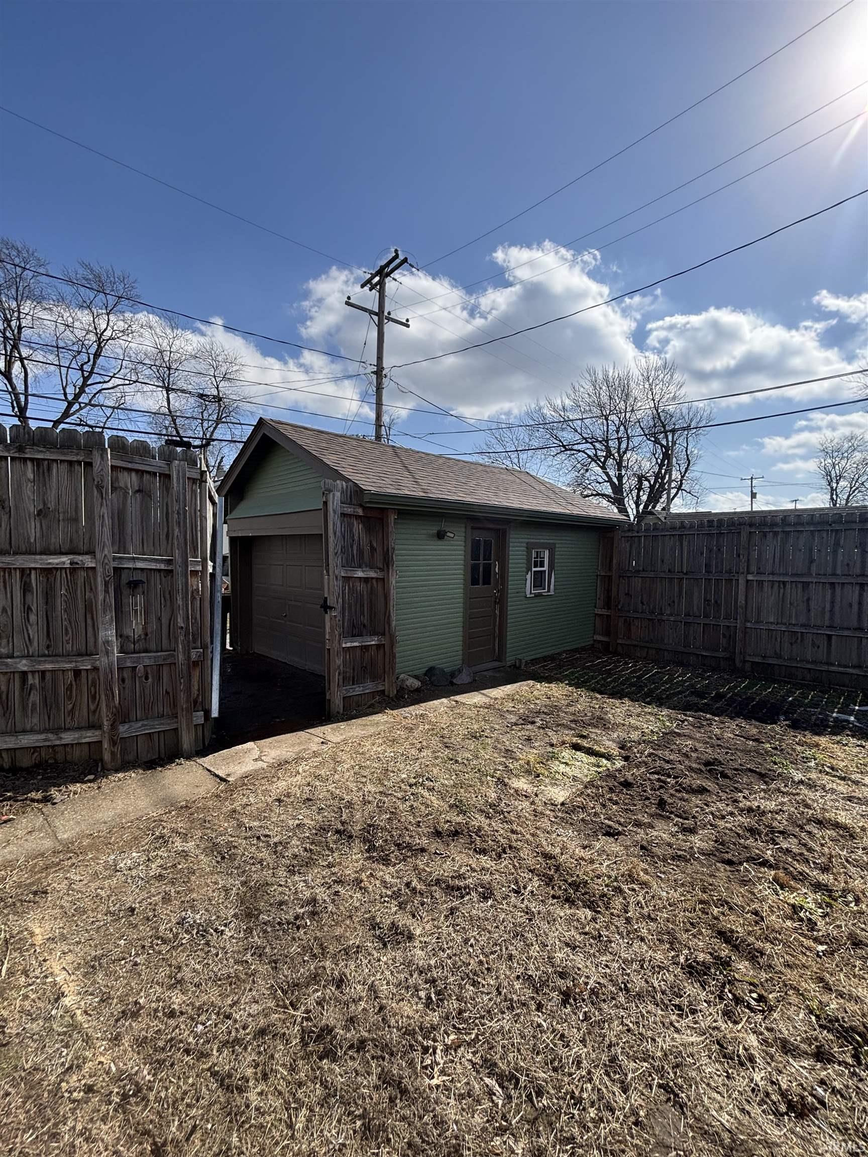 Back of property featuring an outbuilding, a fenced backyard, a detached garage, and a shingled roof