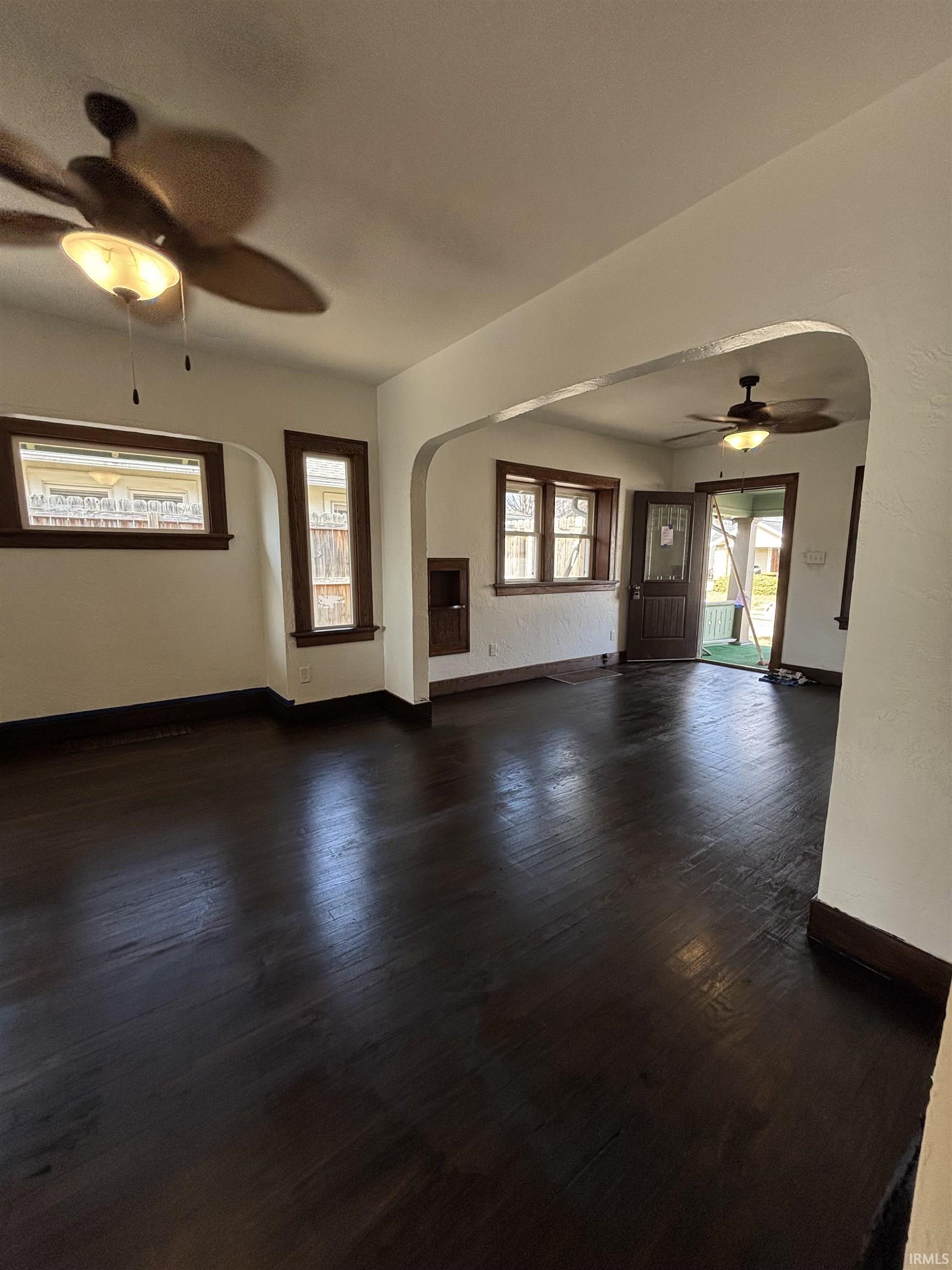 Unfurnished living room with a ceiling fan, arched walkways, dark wood finished floors, and plenty of natural light
