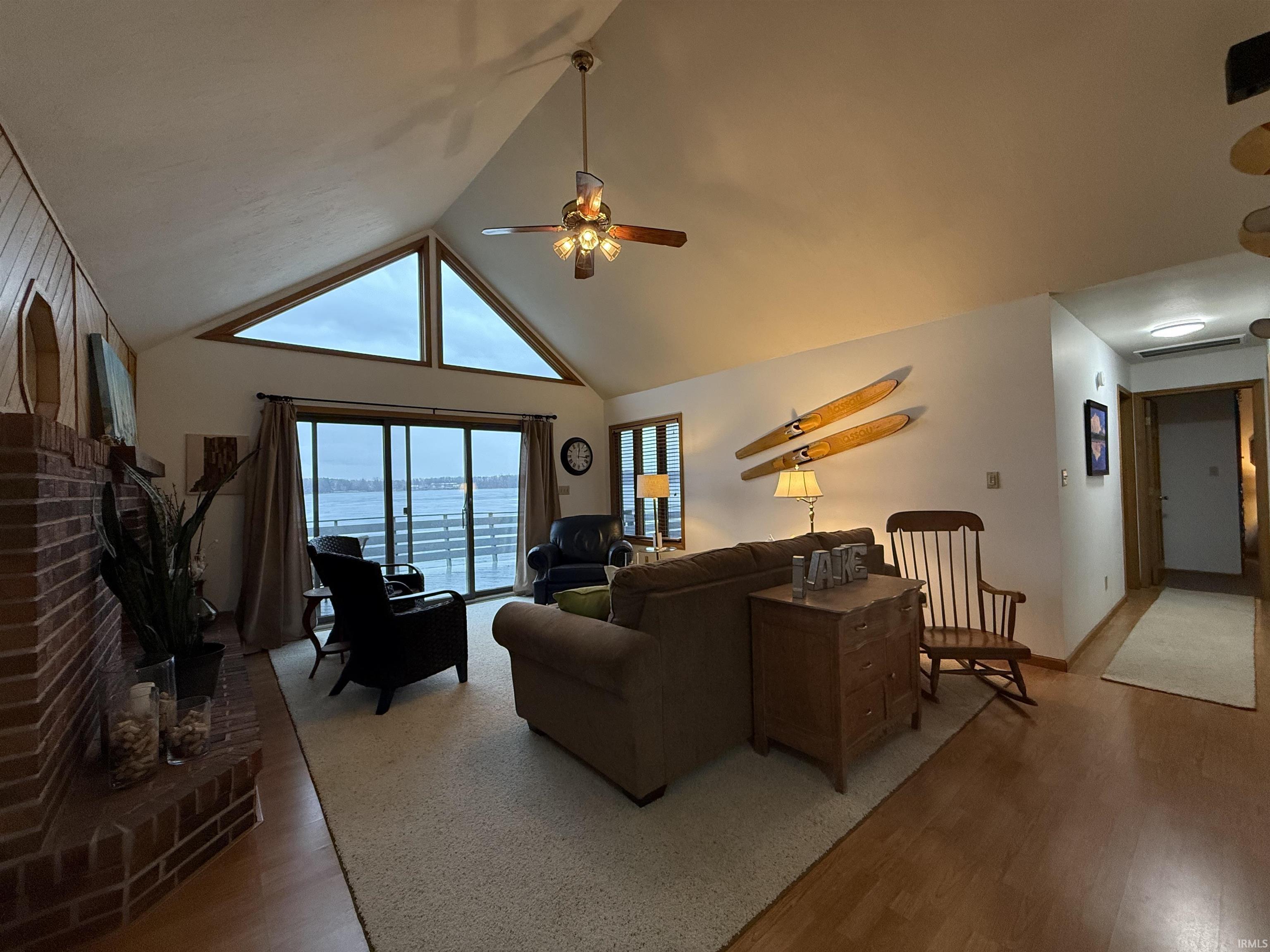 Living area with a high ceiling, wood finished floors, a brick fireplace, a water view, and a ceiling fan