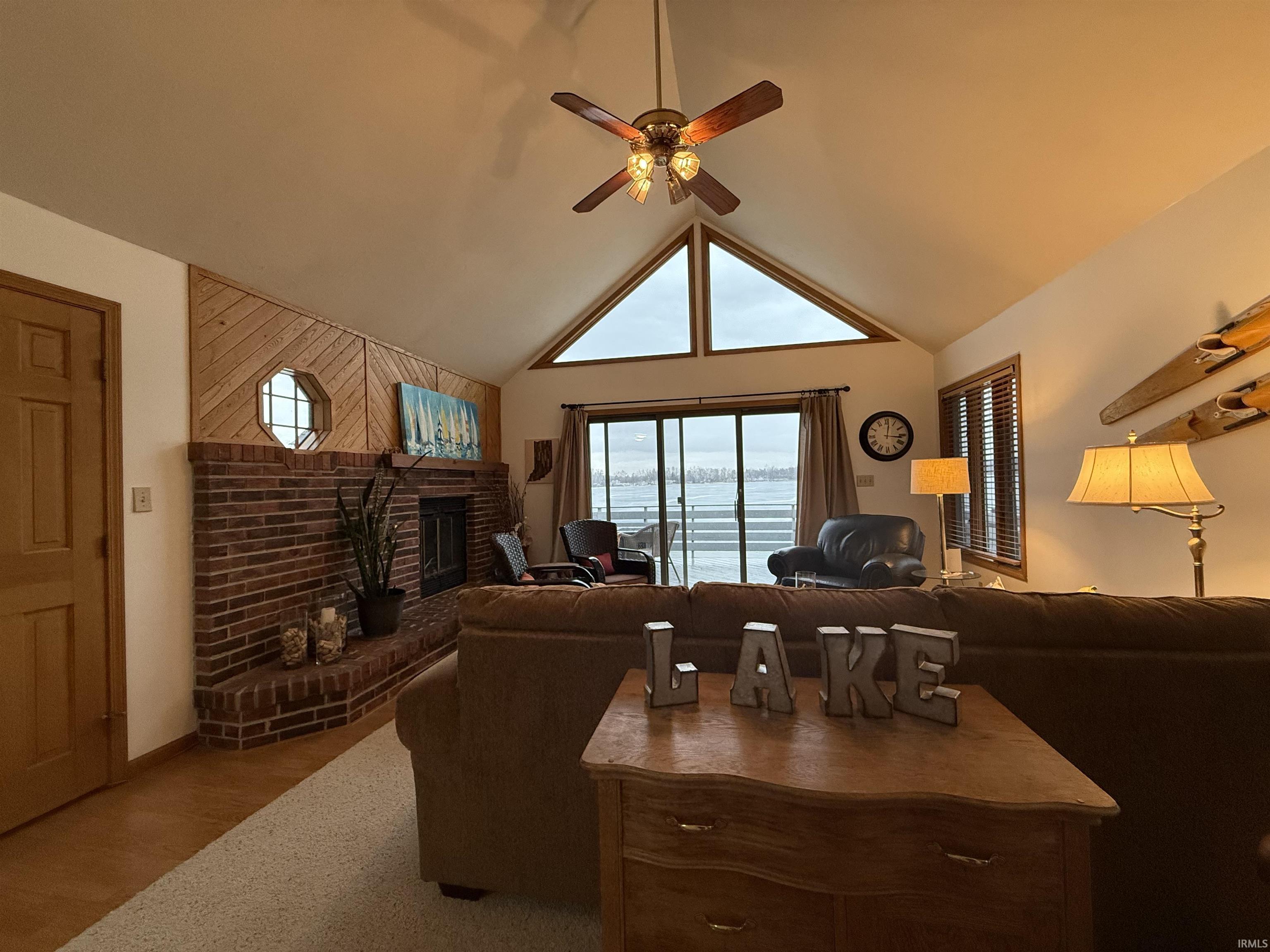 Living area featuring a brick fireplace, light wood-style floors, a ceiling fan, a high ceiling, and a water view