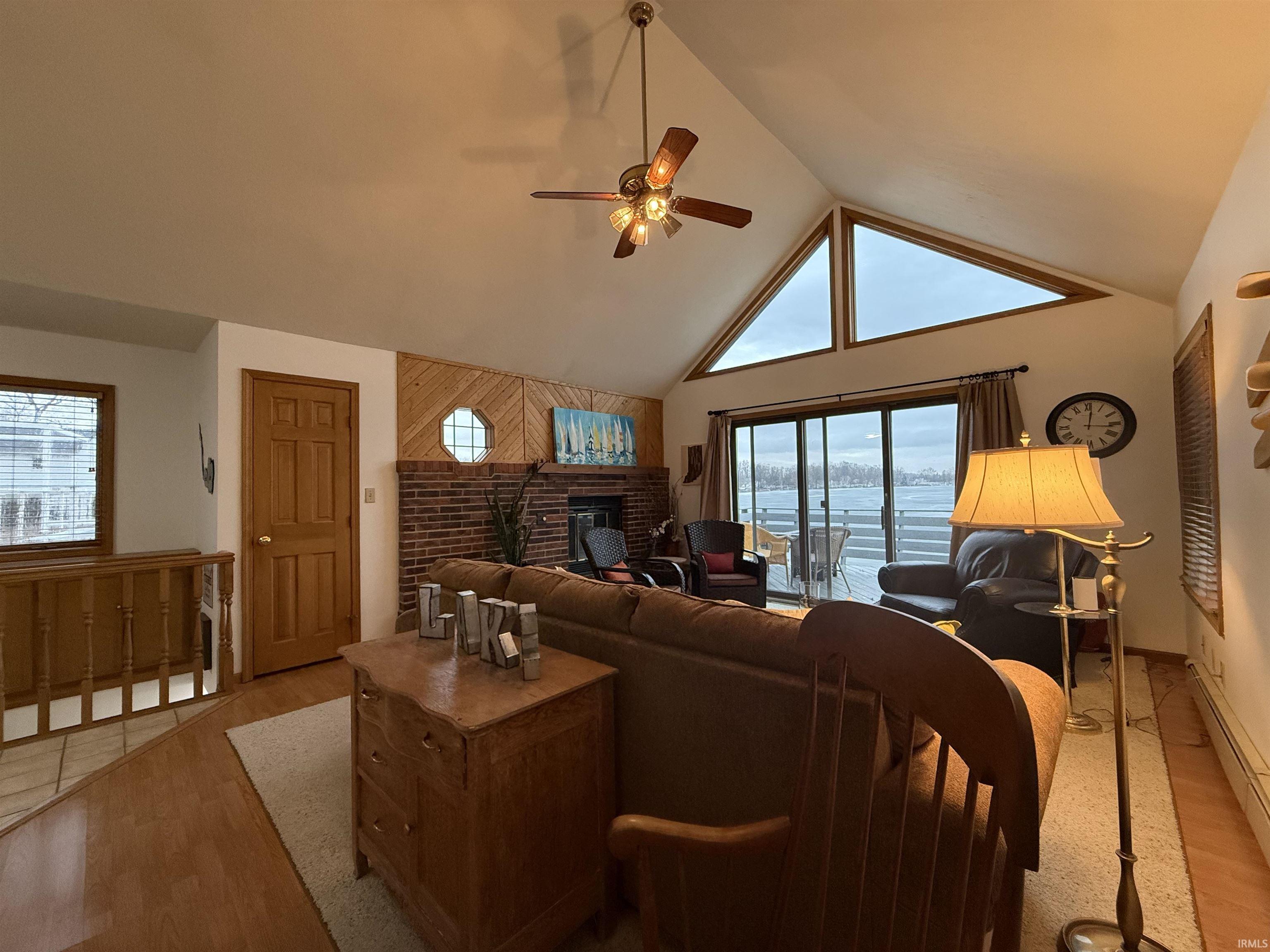 Living area with ceiling fan, a high ceiling, a fireplace, light wood-type flooring, and healthy amount of natural light