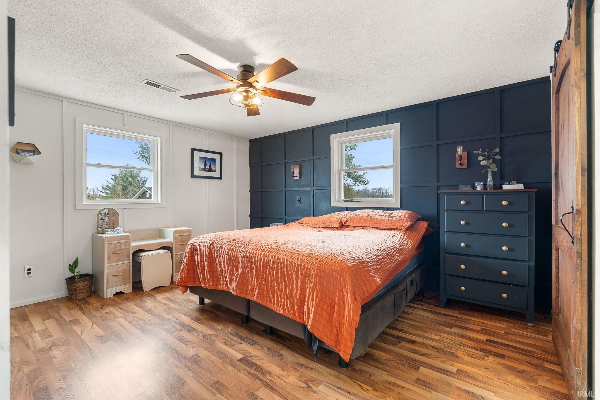 Bedroom featuring a decorative wall, multiple windows, a textured ceiling, wood finished floors, and a barn door