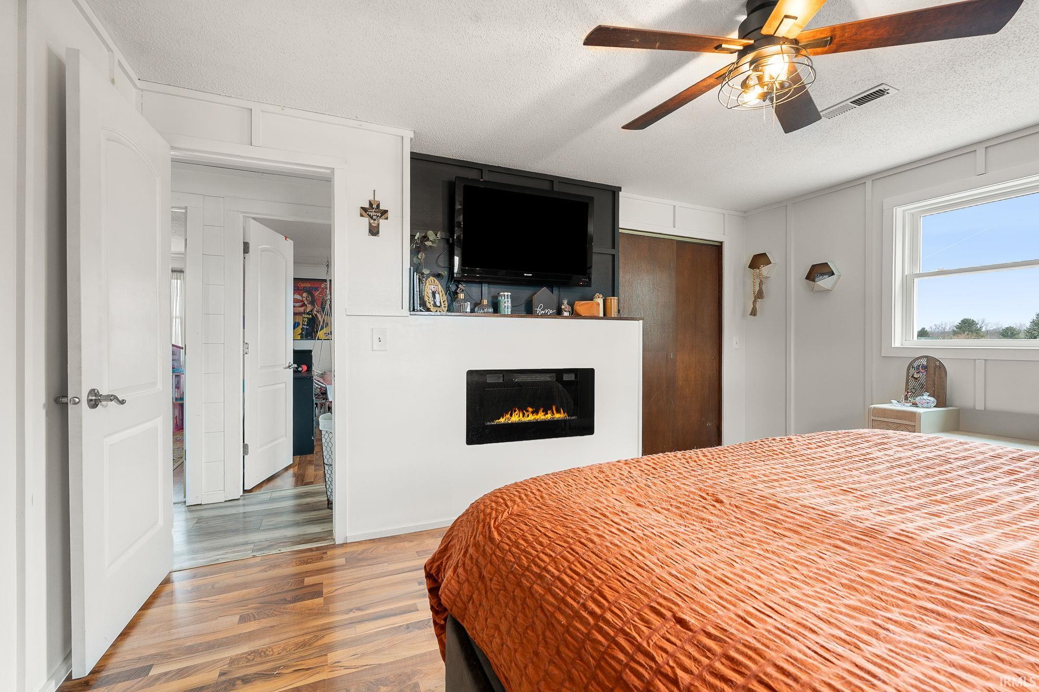 Bedroom featuring wood finished floors, a textured ceiling, a closet, ceiling fan, and a glass covered fireplace