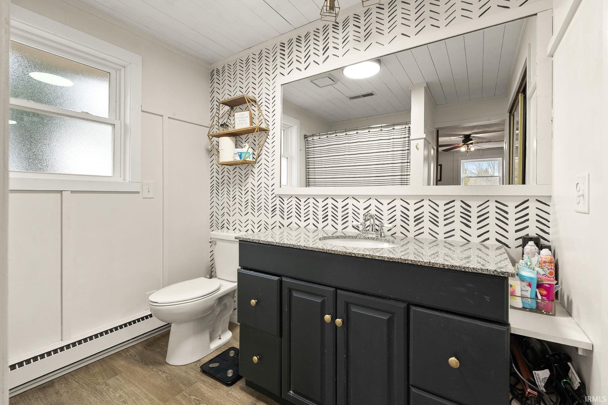 Bathroom with a baseboard heating unit, vanity, backsplash, wood finished floors, and a shower with curtain