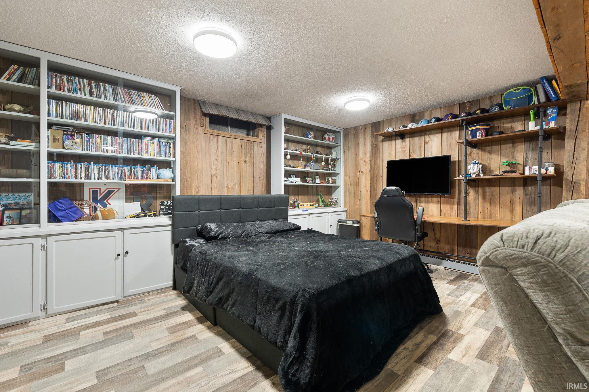 Bedroom featuring a textured ceiling, light wood-style flooring, wooden walls, a baseboard heating unit, and built in desk