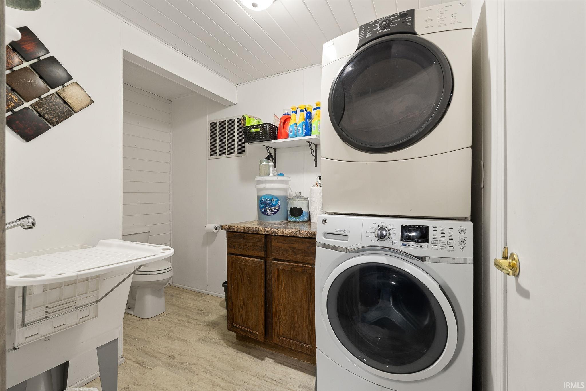 Laundry area with stacked washer and dryer, light wood-style flooring, and wooden ceiling