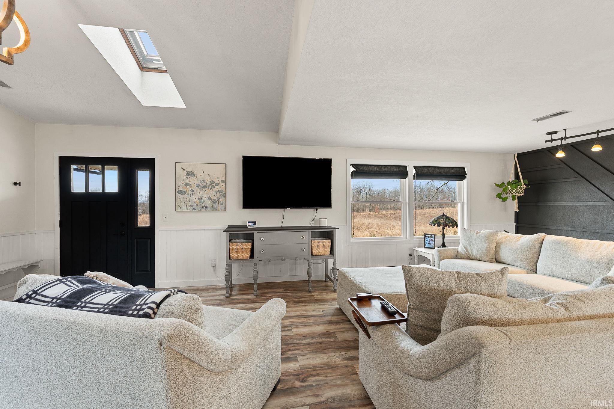 Living area with wood finished floors, wainscoting, healthy amount of natural light, track lighting, and a barn door