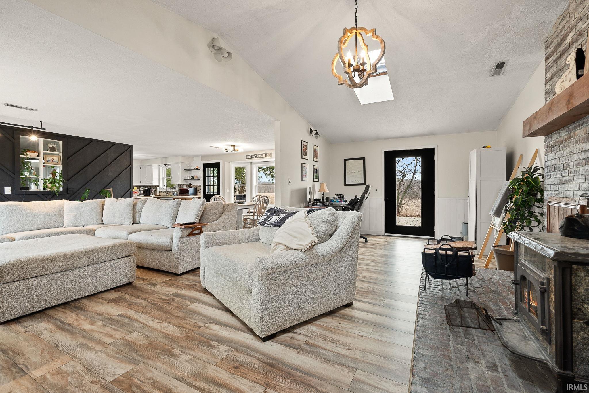 Living area with a fireplace, light wood-type flooring, suspended lighting, and vaulted ceiling