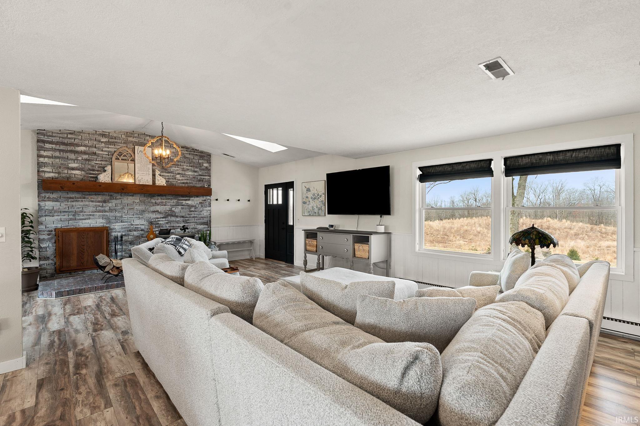 Living room with lofted ceiling, a fireplace, wood finished floors, a skylight, and suspended lighting