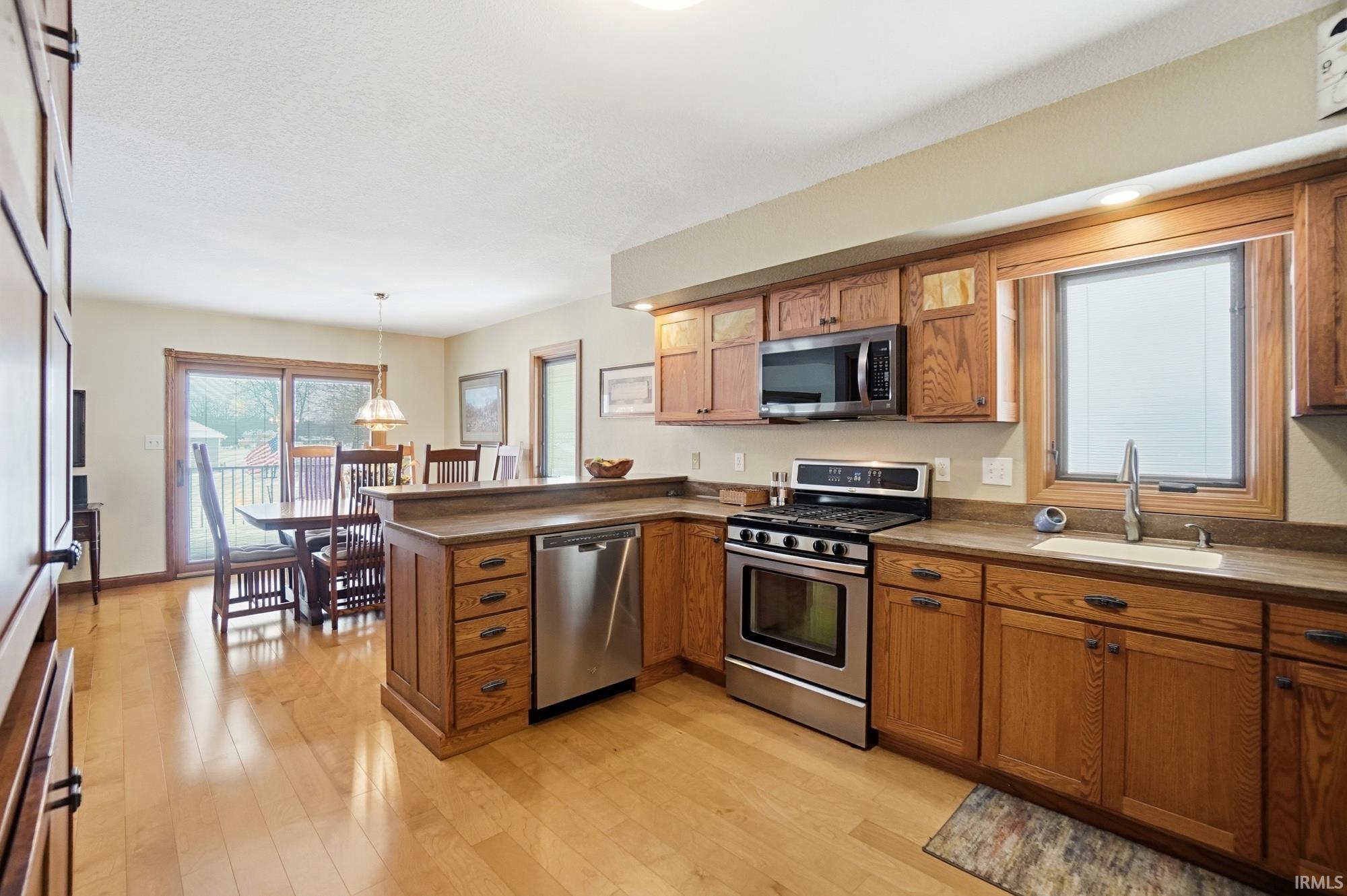 Kitchen with a peninsula, stainless steel appliances, wood finish cabinetry, light wood-style flooring, and decorative light fixtures