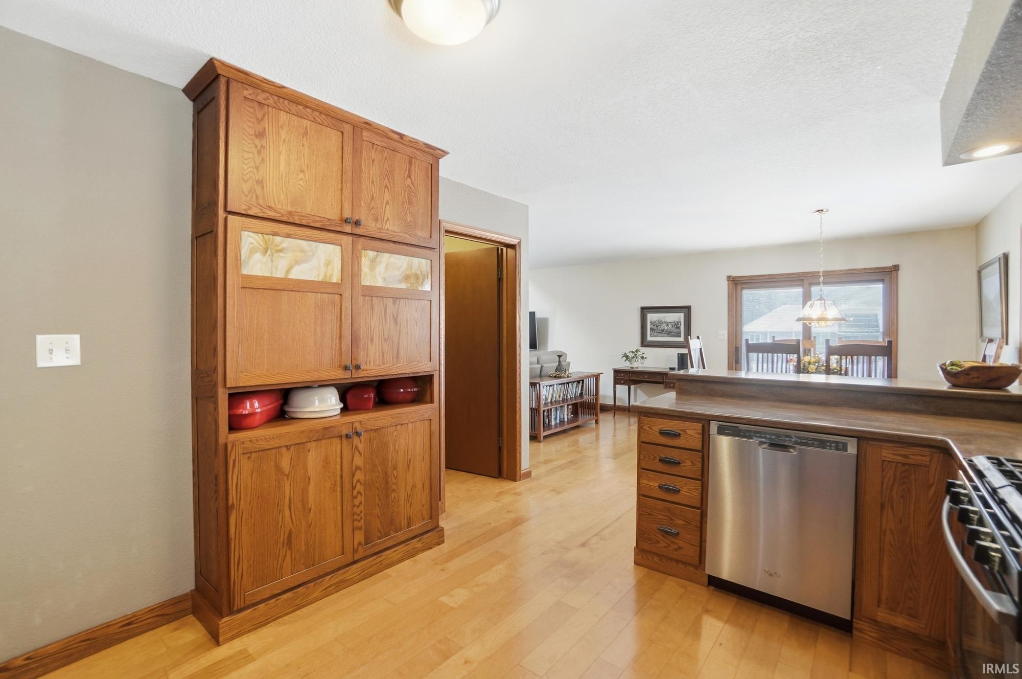 Kitchen featuring stainless steel appliances, light wood-type flooring, dark countertops, wood finish cabinetry, and hanging lights
