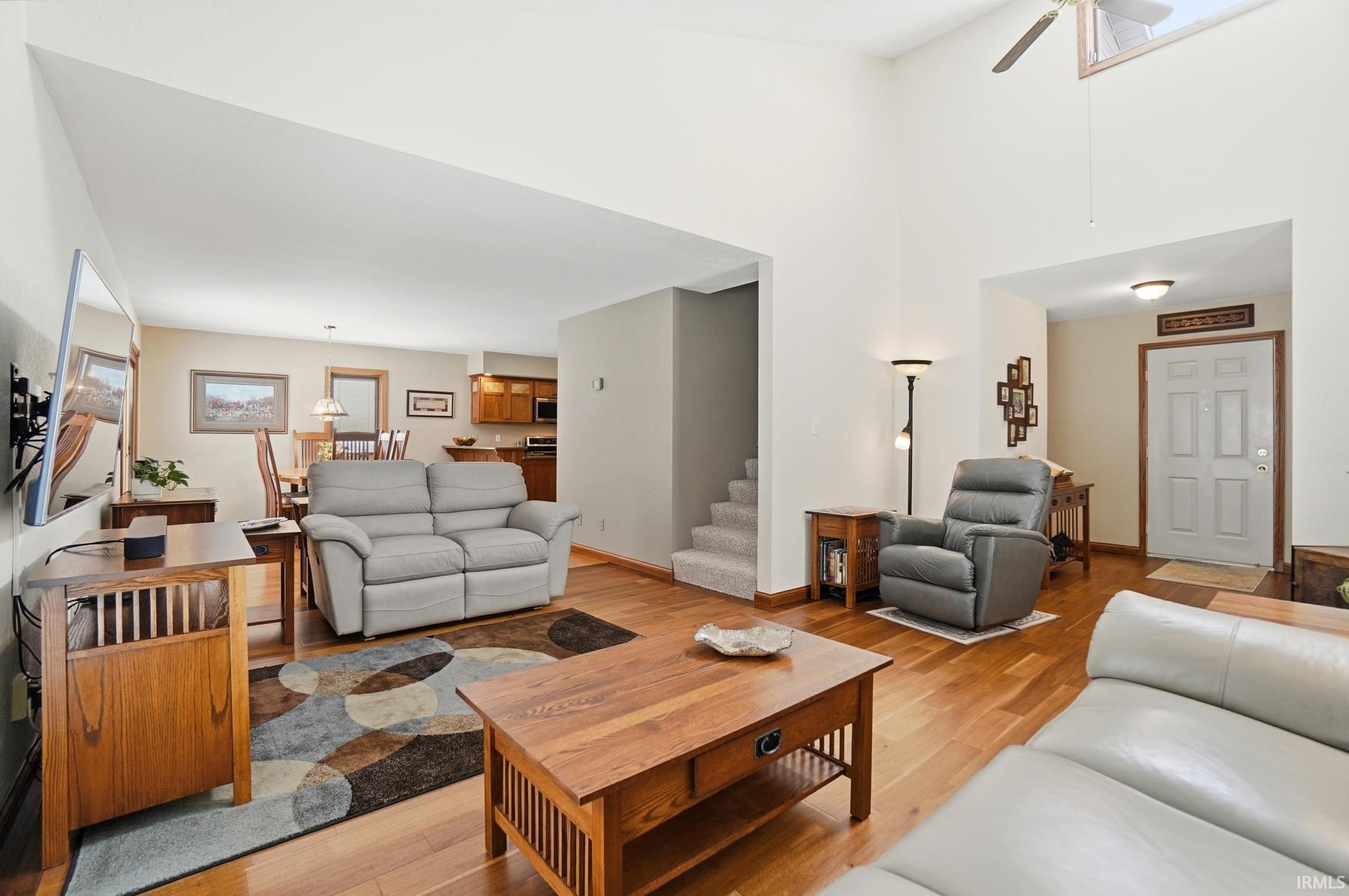 Living room with light wood-type flooring, a ceiling fan, and a high ceiling