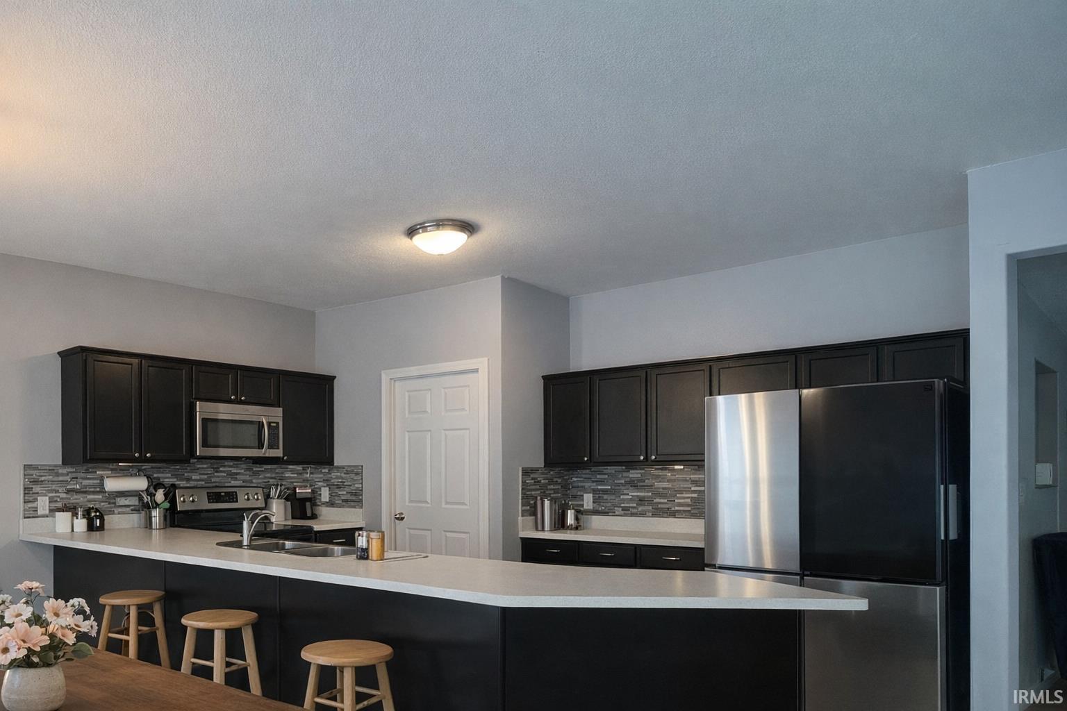 Kitchen with stainless steel appliances, a kitchen breakfast bar, backsplash, a peninsula, and dark cabinetry