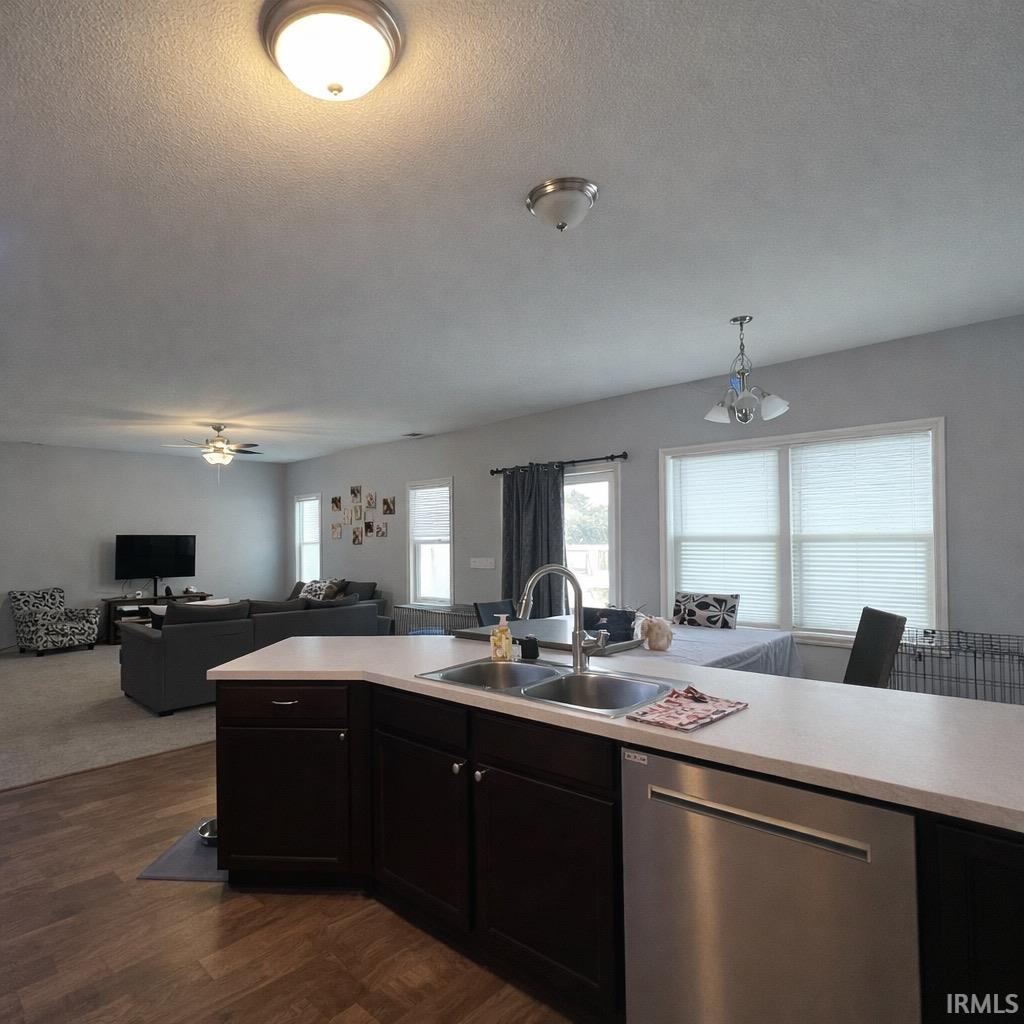 Kitchen with light countertops, stainless steel dishwasher, open floor plan, dark wood-style floors, and a textured ceiling