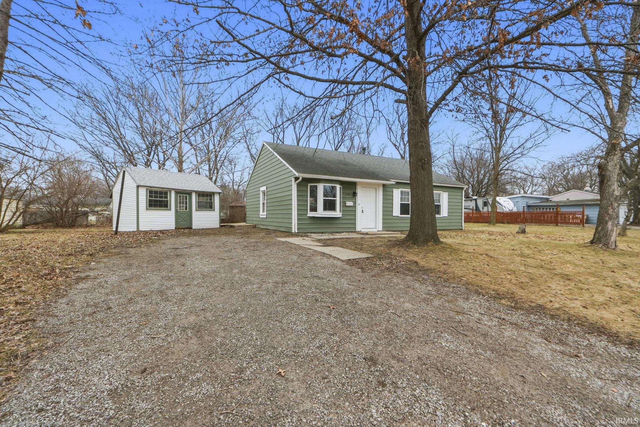 View of front facade with an outbuilding, a shingled roof, and driveway
