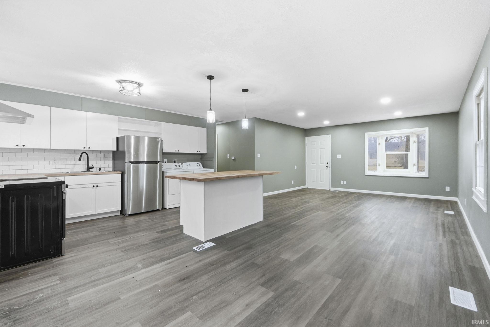 Kitchen featuring white cabinets, a kitchen island, freestanding refrigerator, washer / dryer, and decorative light fixtures