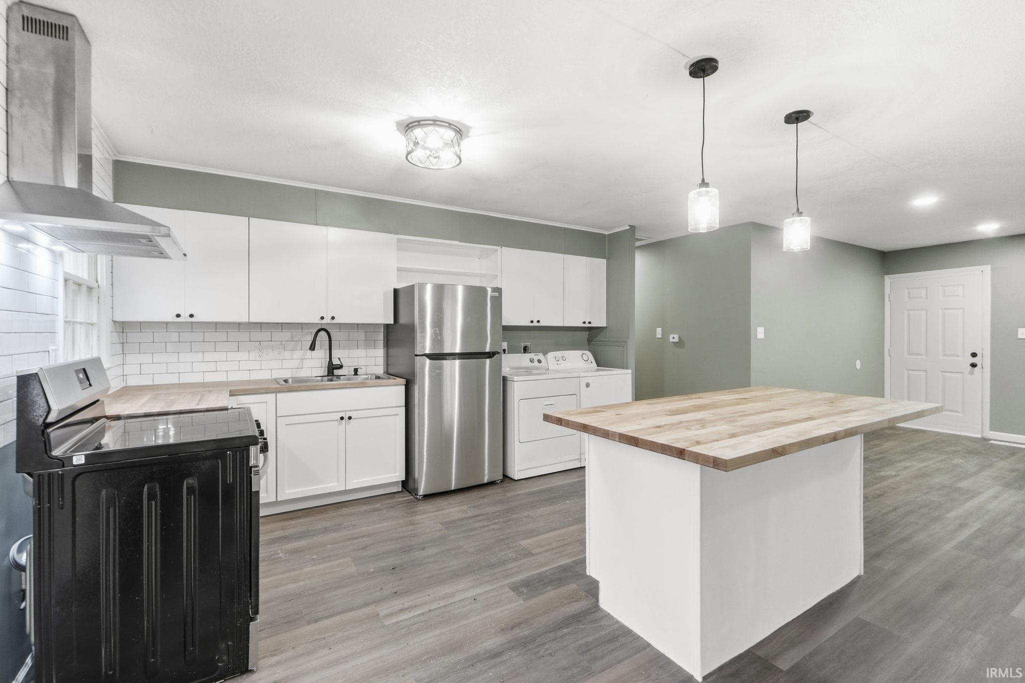 Kitchen with butcher block counters, range with electric cooktop, white cabinetry, freestanding refrigerator, and a center island