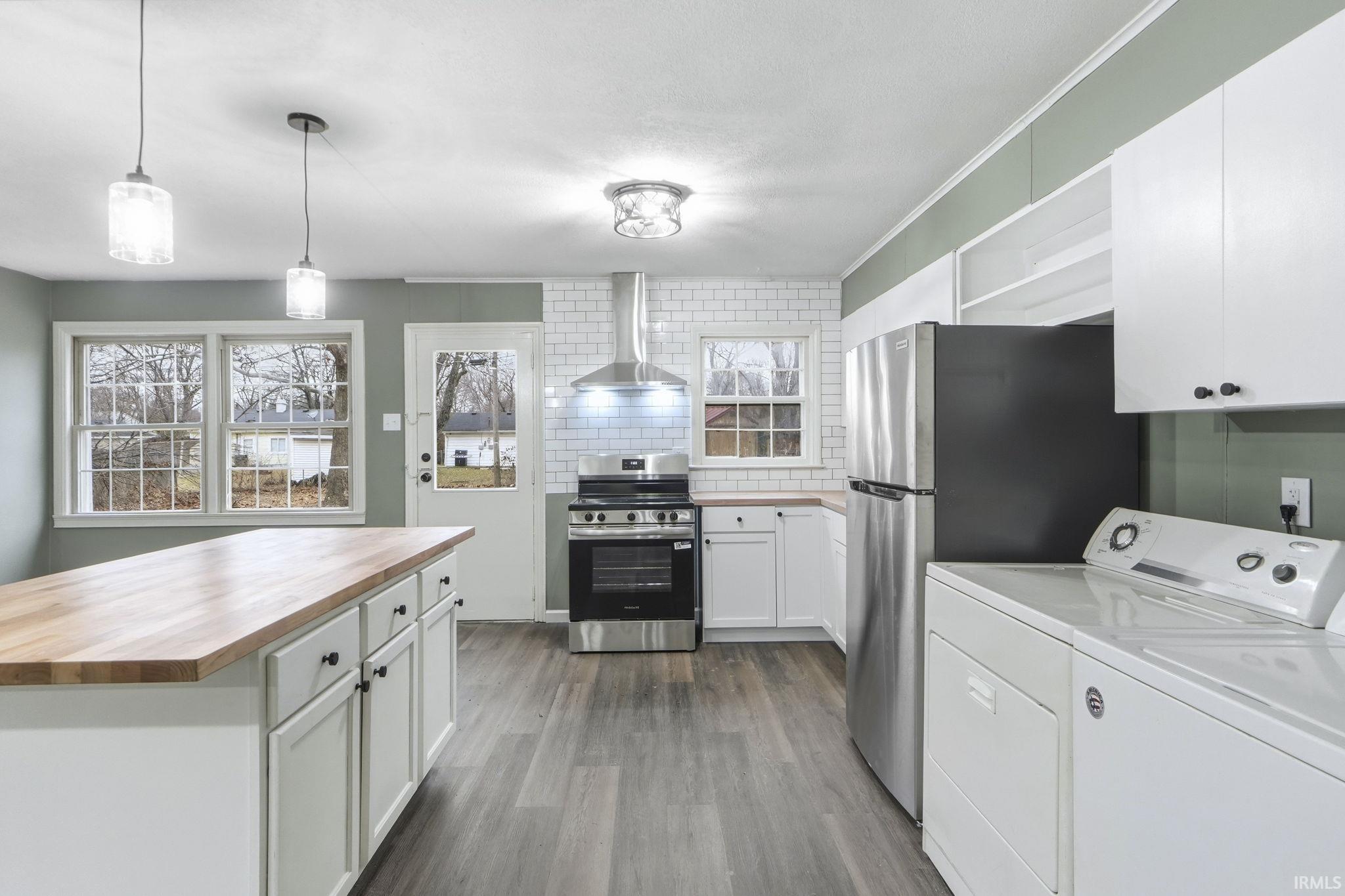 Kitchen featuring butcher block counters, stainless steel appliances, white cabinetry, decorative backsplash, and pendant lighting