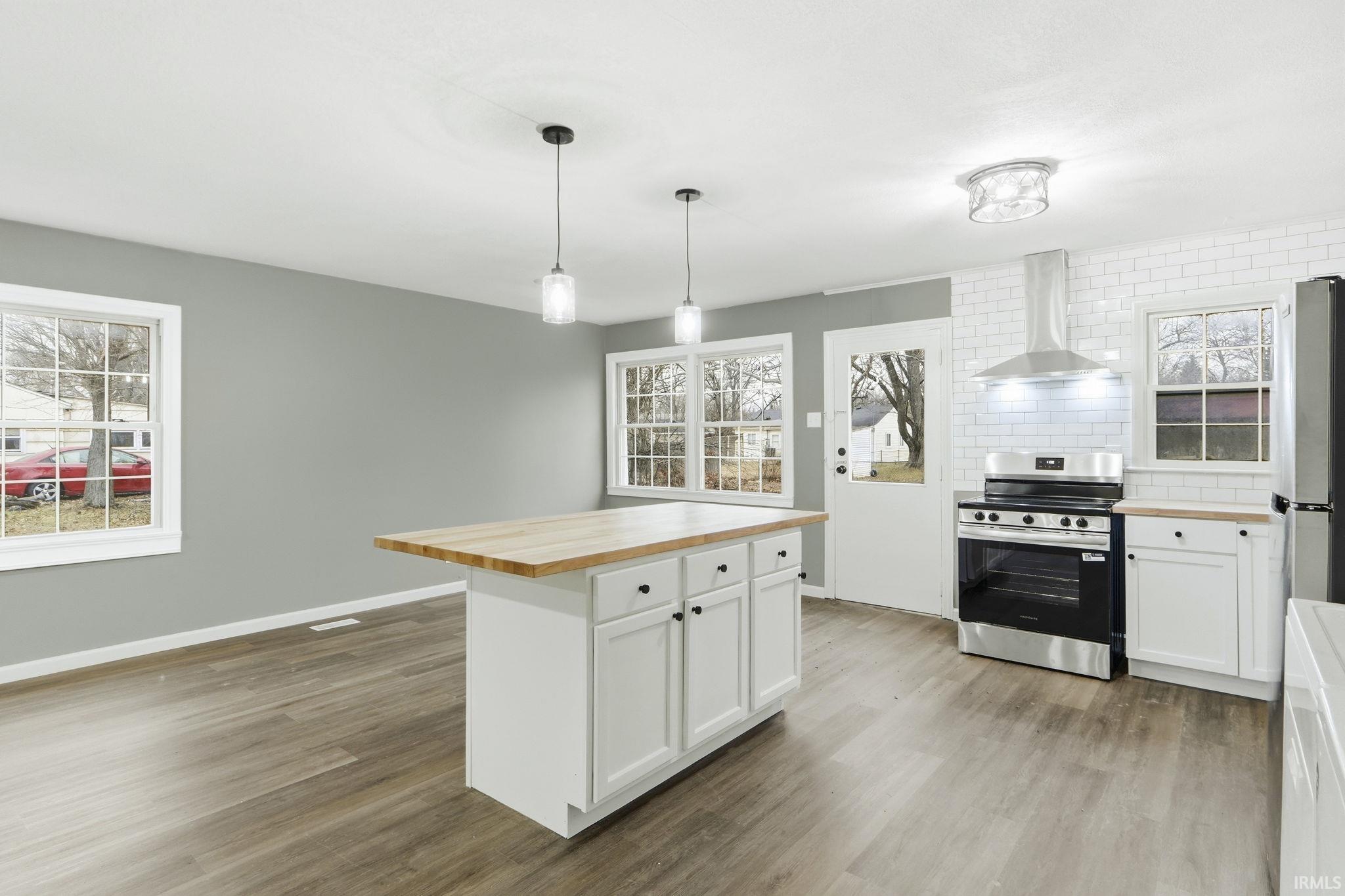 Kitchen with wood counters, white cabinets, stainless steel appliances, hanging light fixtures, and tasteful backsplash