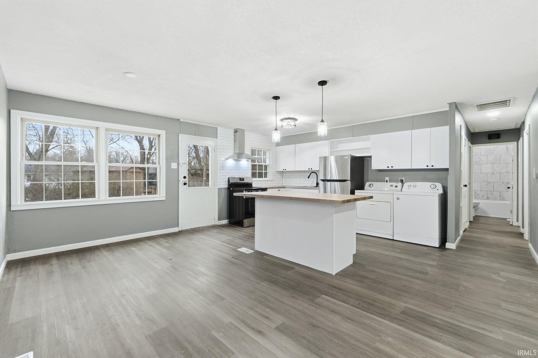 Kitchen with white cabinets, a kitchen island, butcher block countertops, hanging light fixtures, and stainless steel appliances