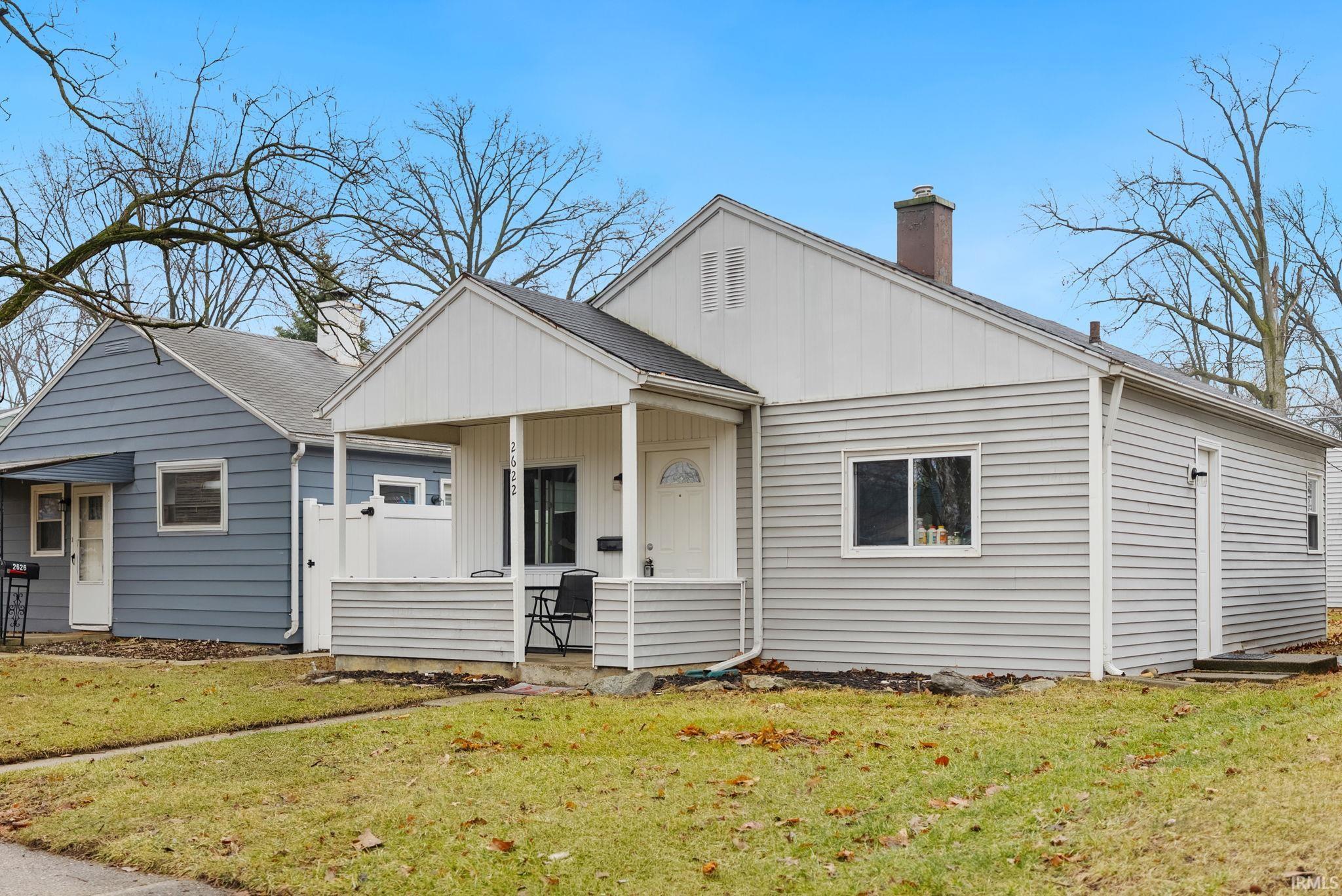 Bungalow-style home with a chimney, a front lawn, covered porch, and a shingled roof