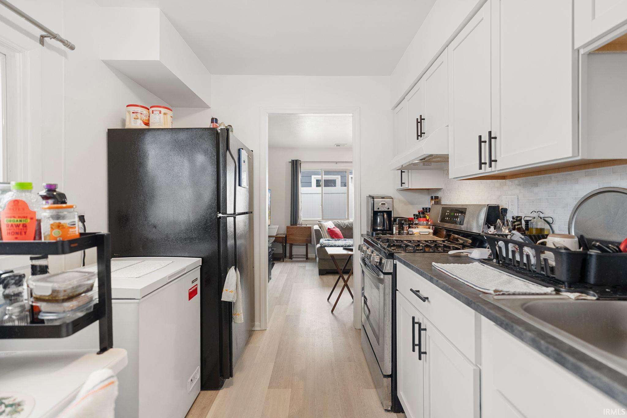 Kitchen with stainless steel gas range oven, freestanding refrigerator, light wood-style floors, and white cabinetry