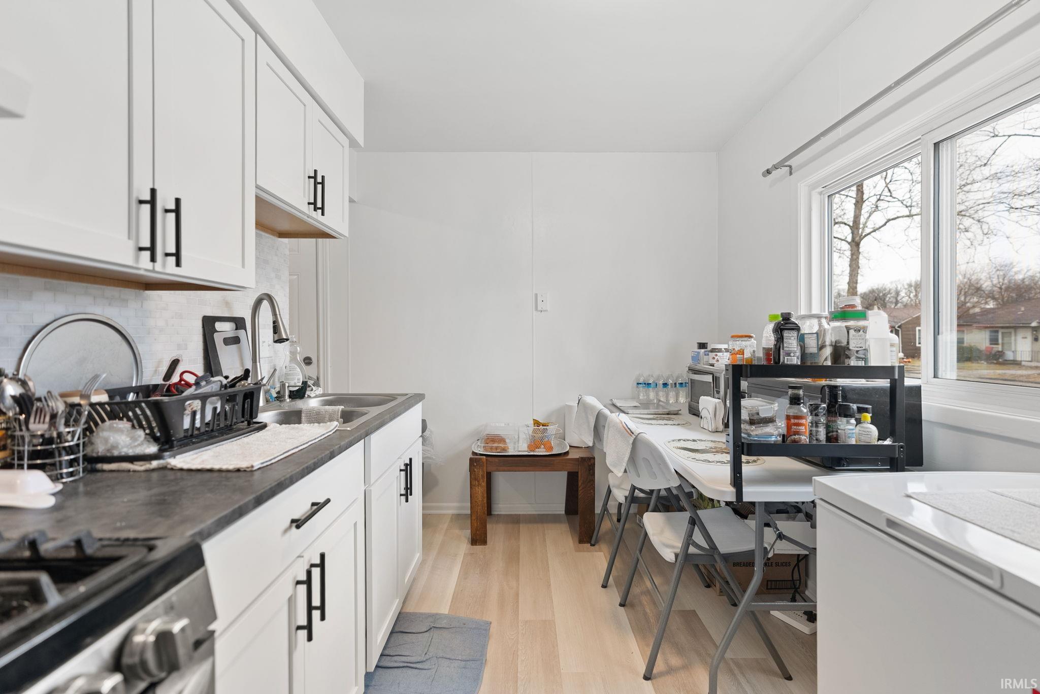 Kitchen with stainless steel gas stove, light wood-style floors, white fridge, dark countertops, and white cabinets