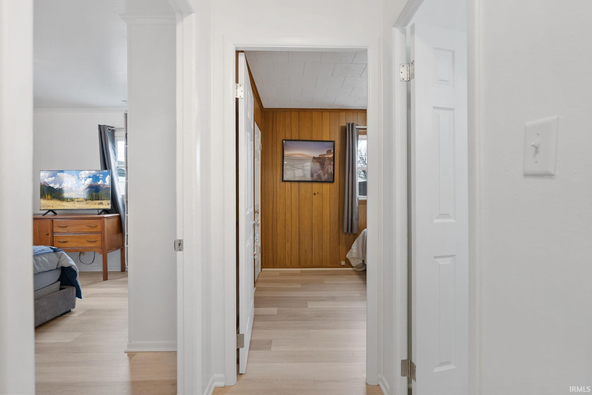 Corridor featuring light wood-style flooring, wooden walls, and ornamental molding