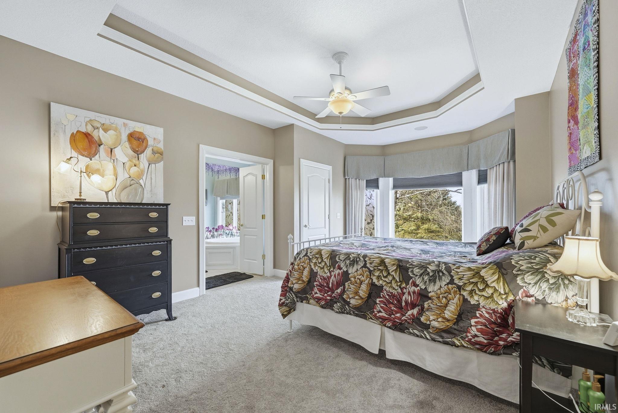 Bedroom with light carpet, a tray ceiling, connected bathroom, and a ceiling fan