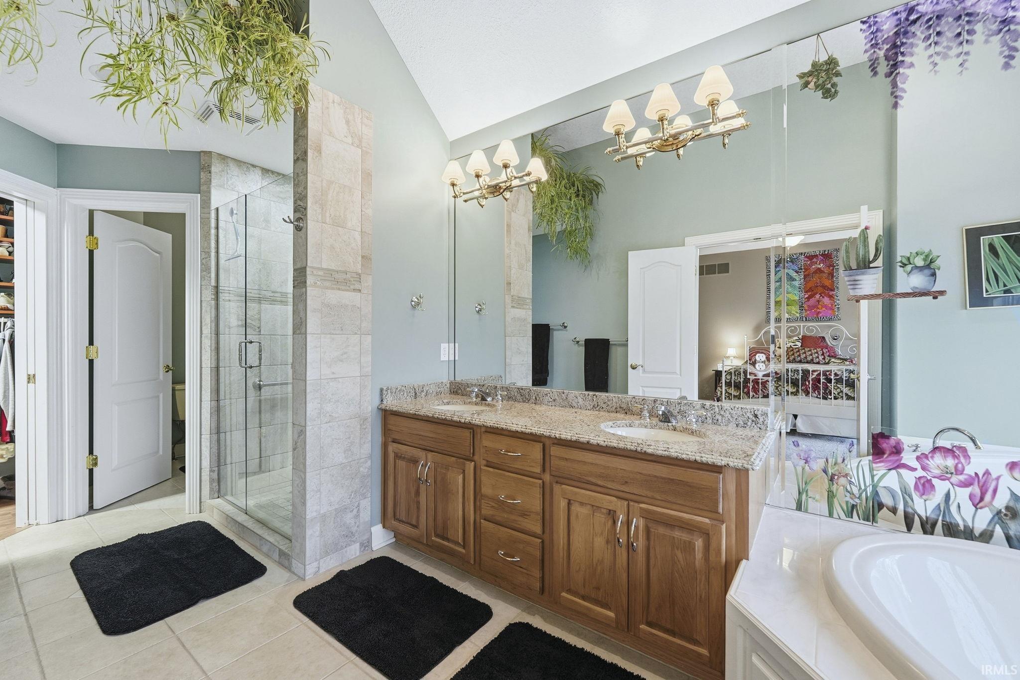 Full bath with double vanity, light tile patterned floors, a bath, a shower stall, and lofted ceiling