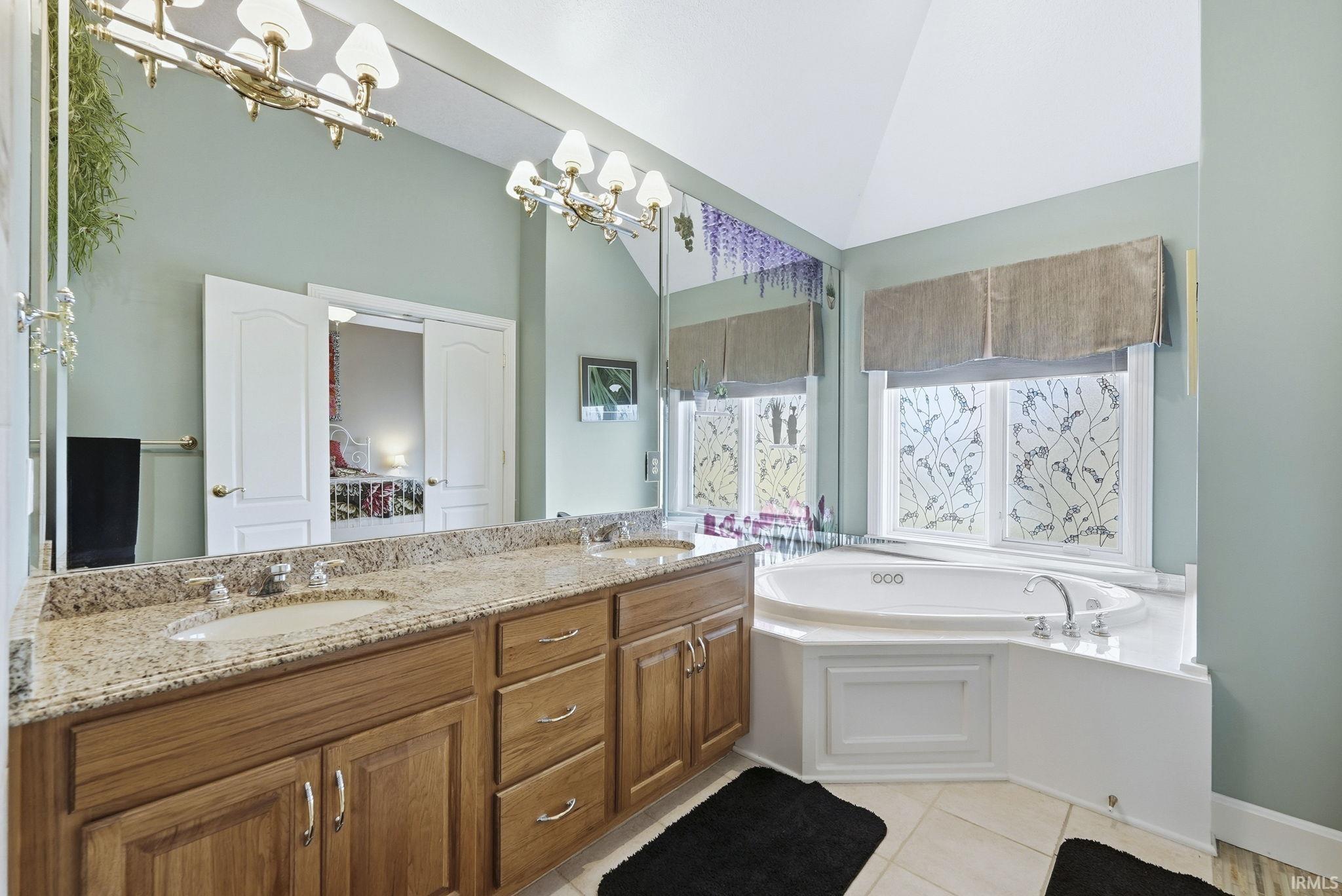 Full bath featuring double vanity, a bath, a chandelier, vaulted ceiling, and light tile patterned floors