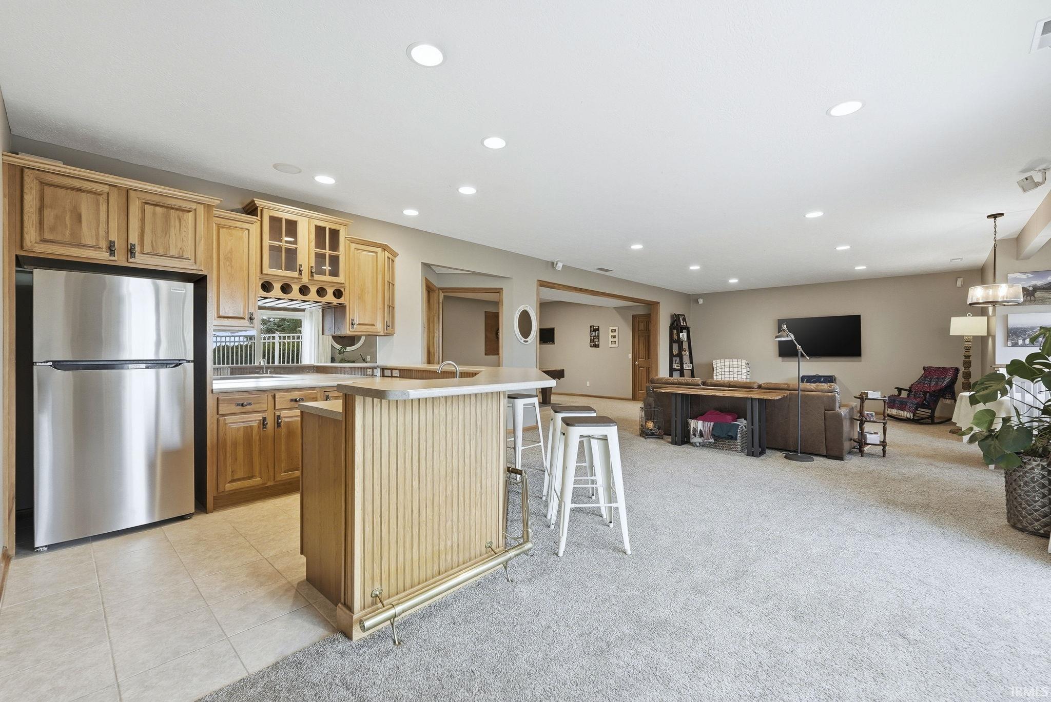 Kitchen with glass fronted cabinets, freestanding refrigerator, a kitchen bar, light colored carpet, and light countertops