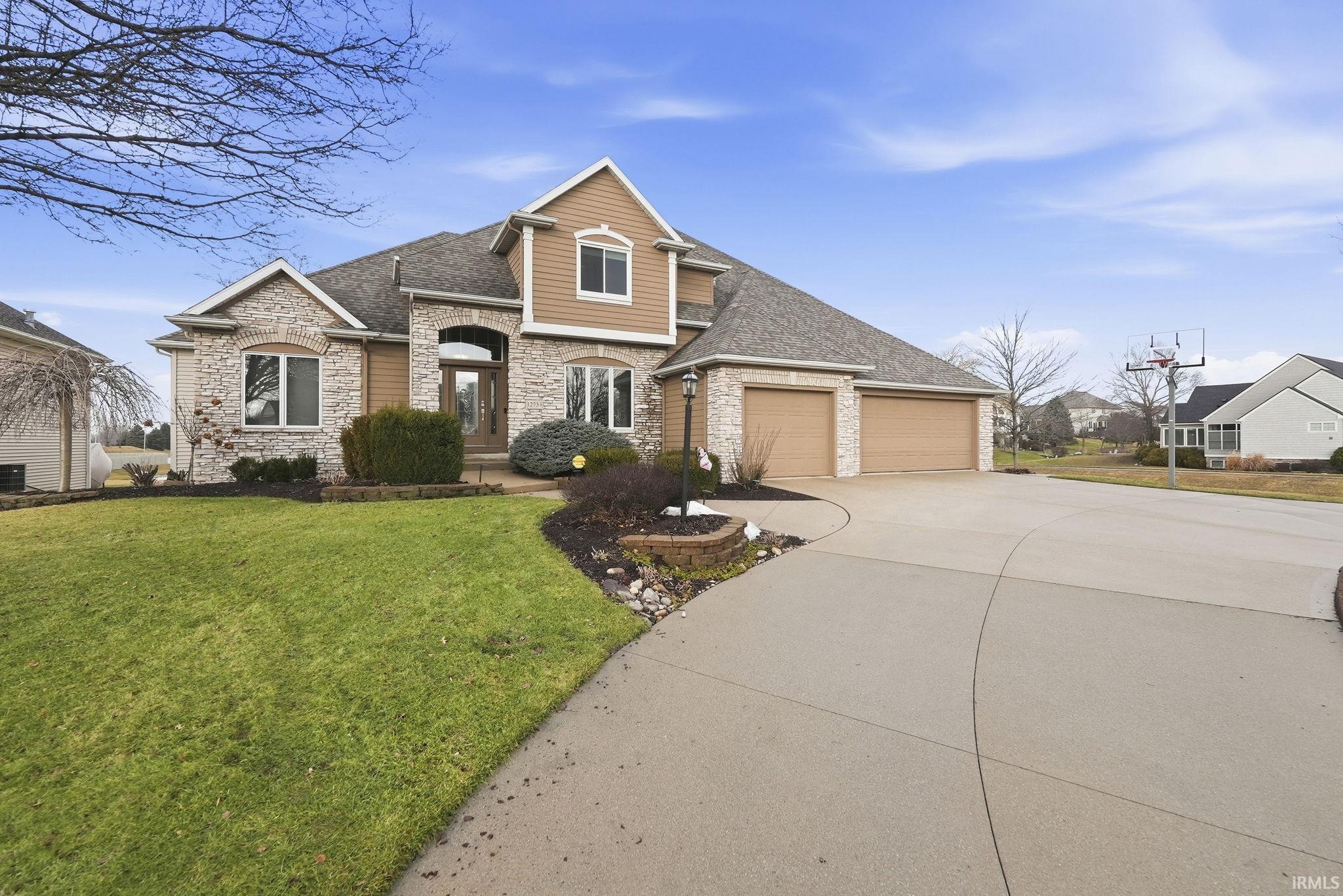 View of front facade featuring stone siding, roof with shingles, concrete driveway, and a front lawn