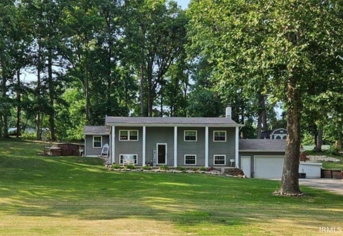Raised ranch featuring covered porch, a chimney, a front lawn, a garage, and view of scattered trees