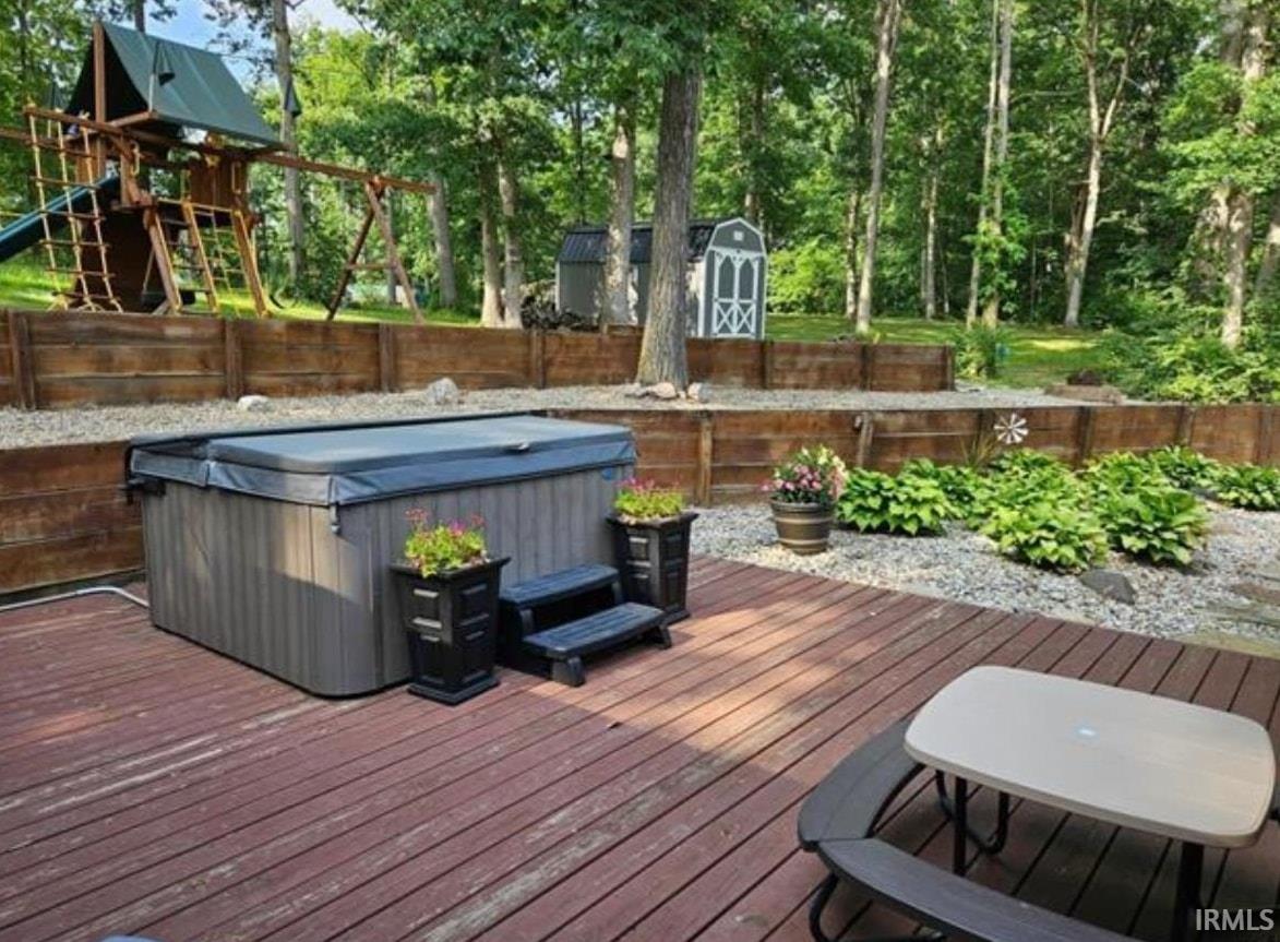 Deck featuring a fenced backyard, a shed, a hot tub, and a playground