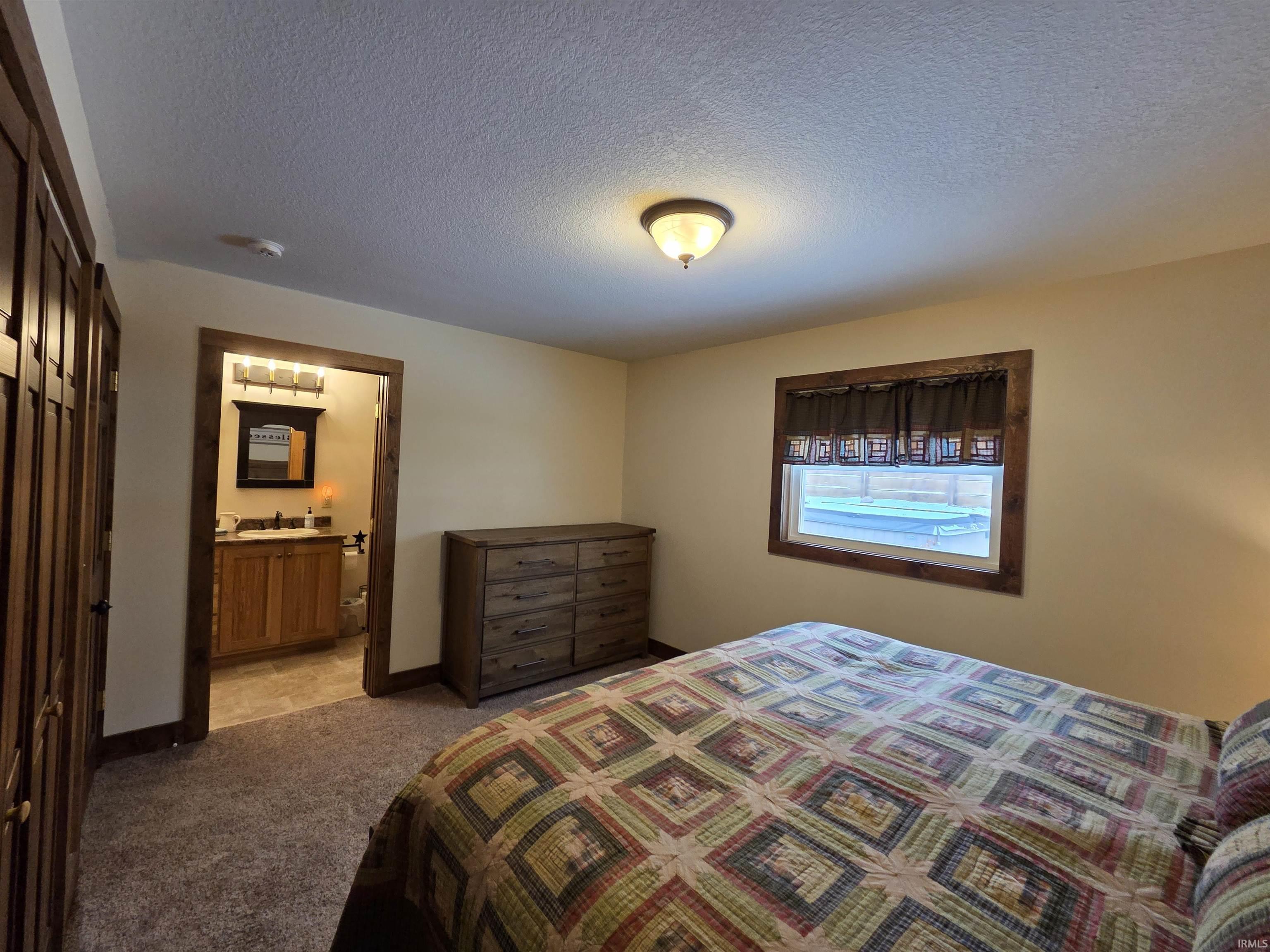 Bedroom with a textured ceiling, carpet, and connected bathroom