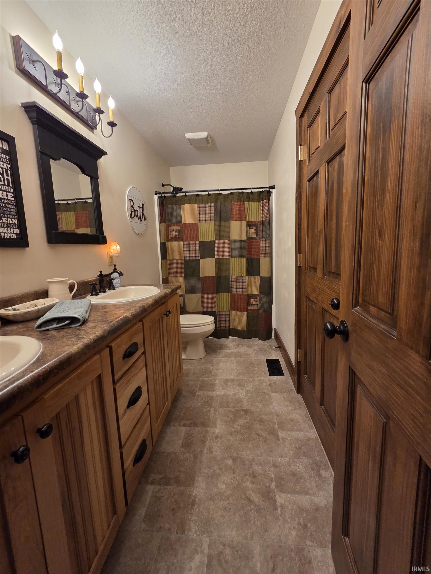 Full bath featuring a shower with curtain, double vanity, stone finish floors, and a textured ceiling