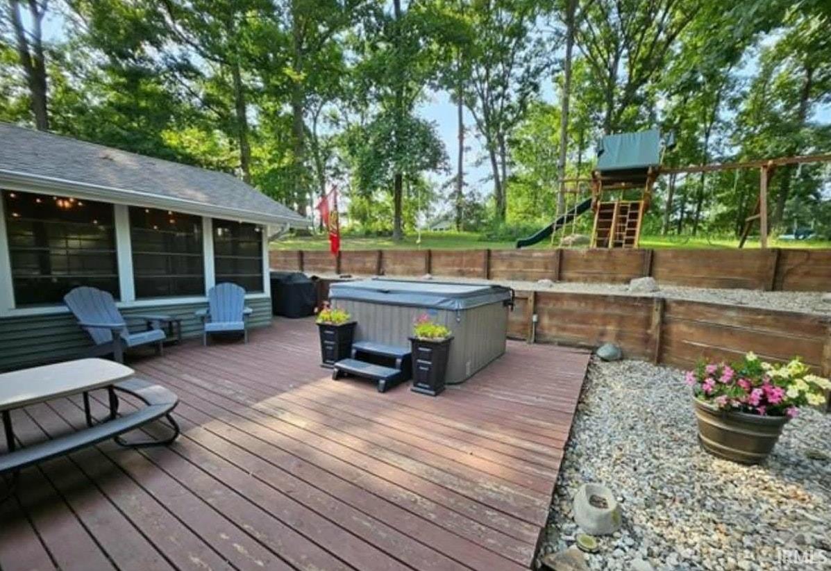 Deck featuring a hot tub, a fenced backyard, and a sunroom