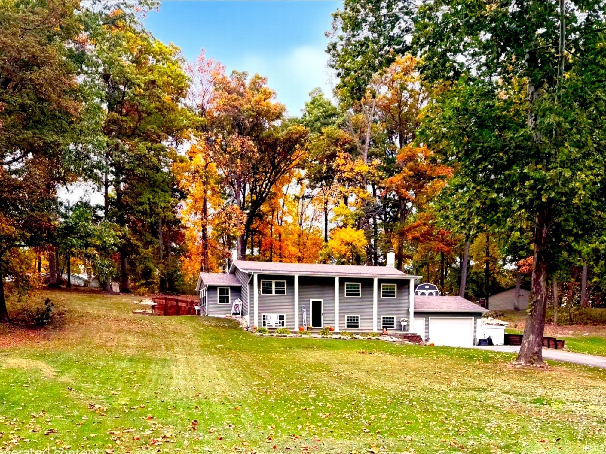 Raised ranch featuring a front yard, a garage, view of scattered trees, and a chimney