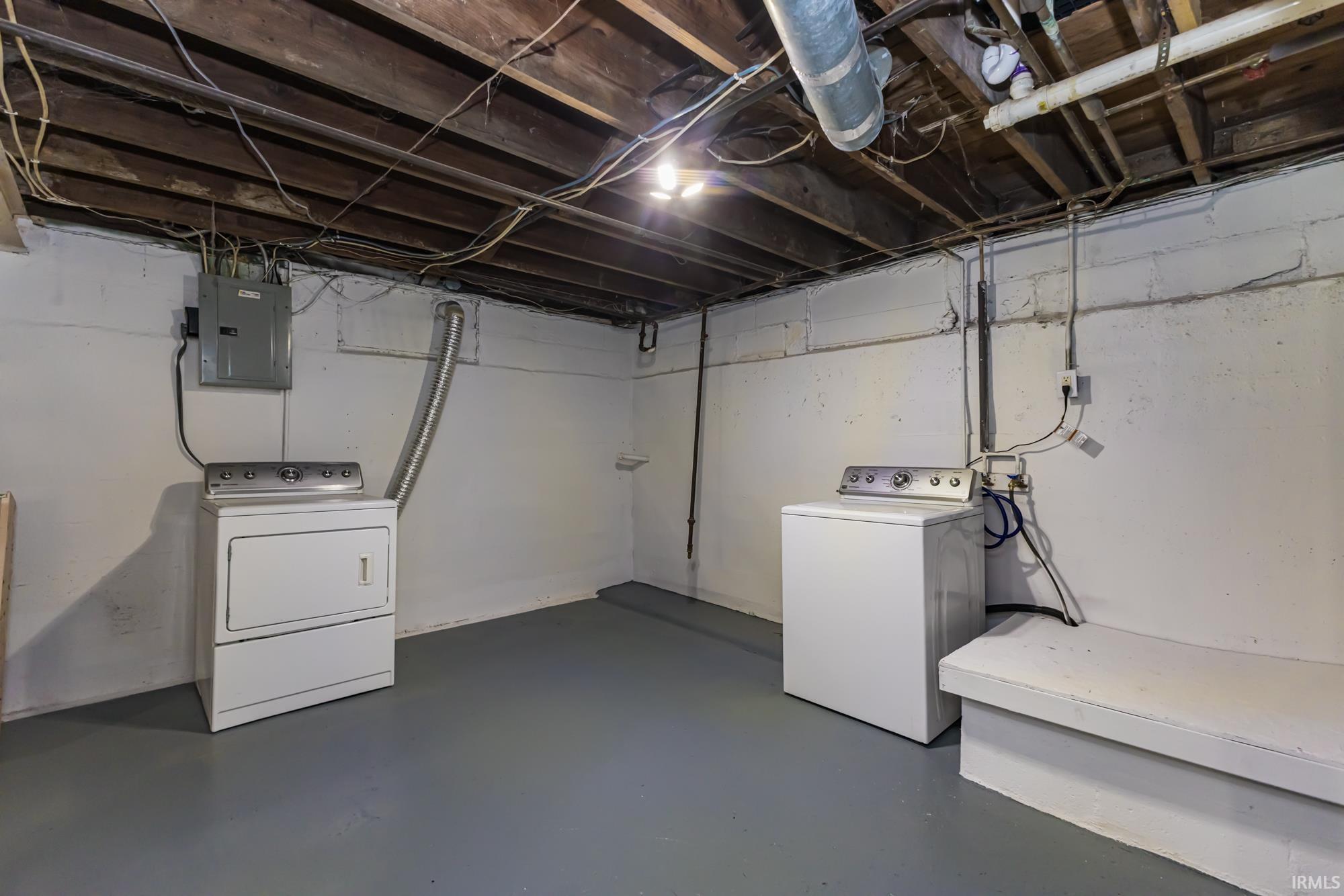 Unfinished below grade area with electric panel and independent washer and dryer