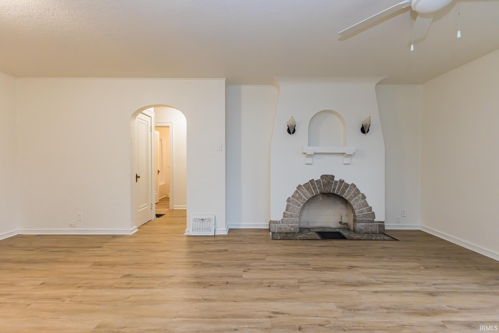 Unfurnished living room featuring light wood-style floors, a fireplace with flush hearth, arched walkways, and a ceiling fan