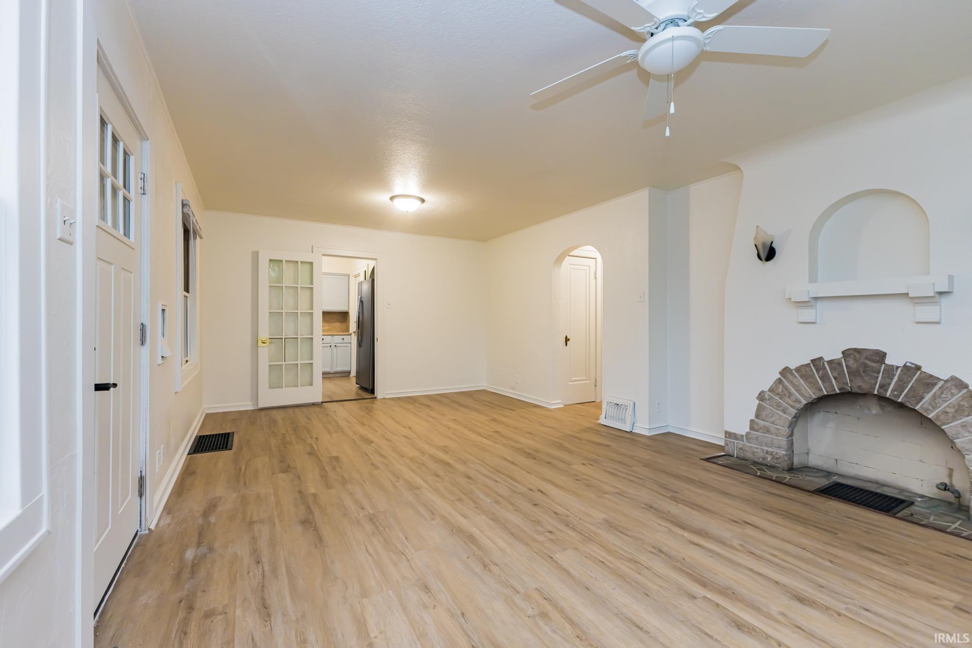 Unfurnished living room with light wood-style flooring, arched walkways, a ceiling fan, and a fireplace with flush hearth