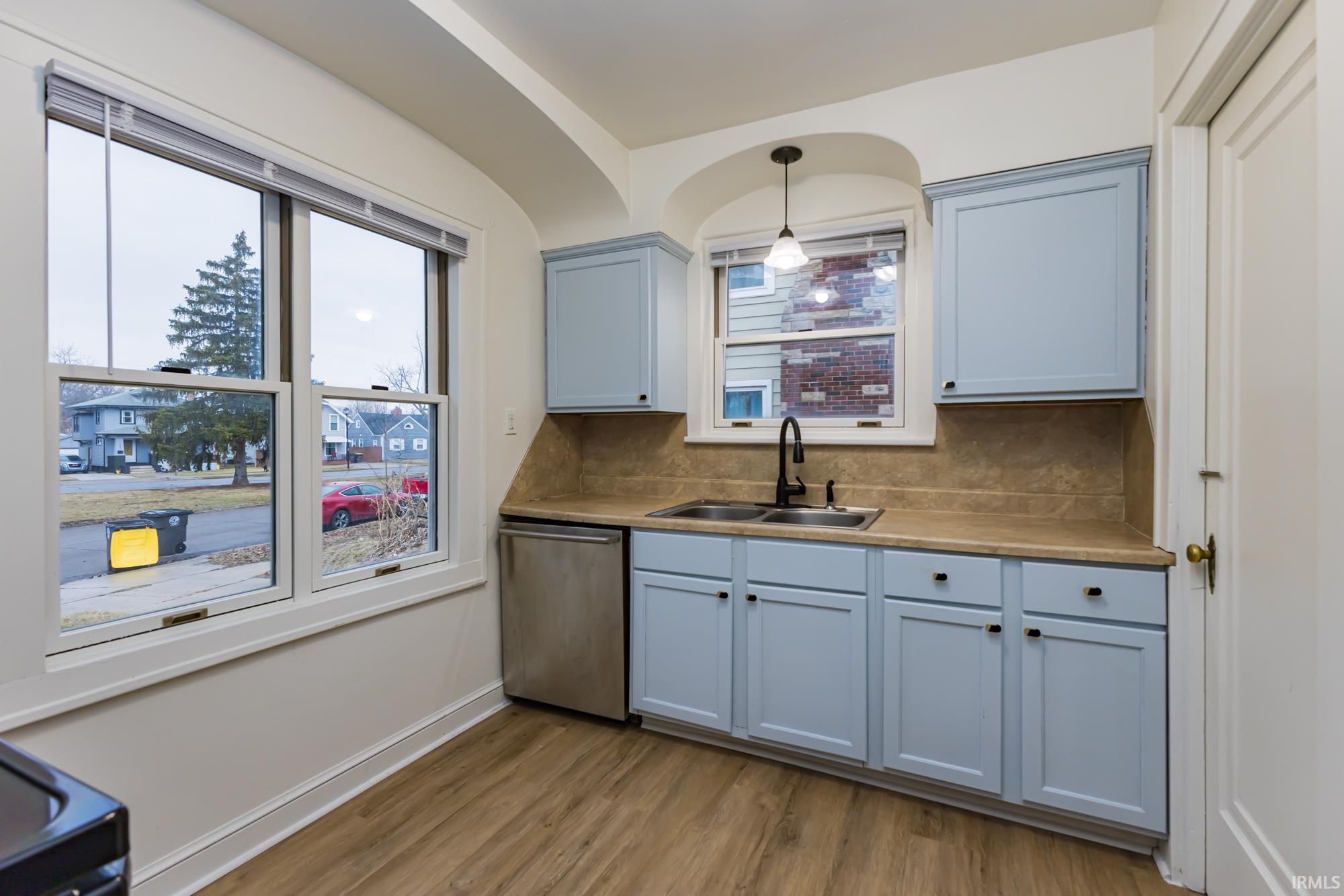 Kitchen featuring decorative light fixtures, dishwasher, light wood finished floors, tasteful backsplash, and light countertops