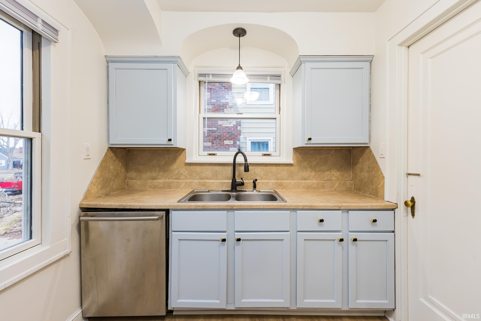 Kitchen with stainless steel dishwasher, light countertops, pendant lighting, and backsplash