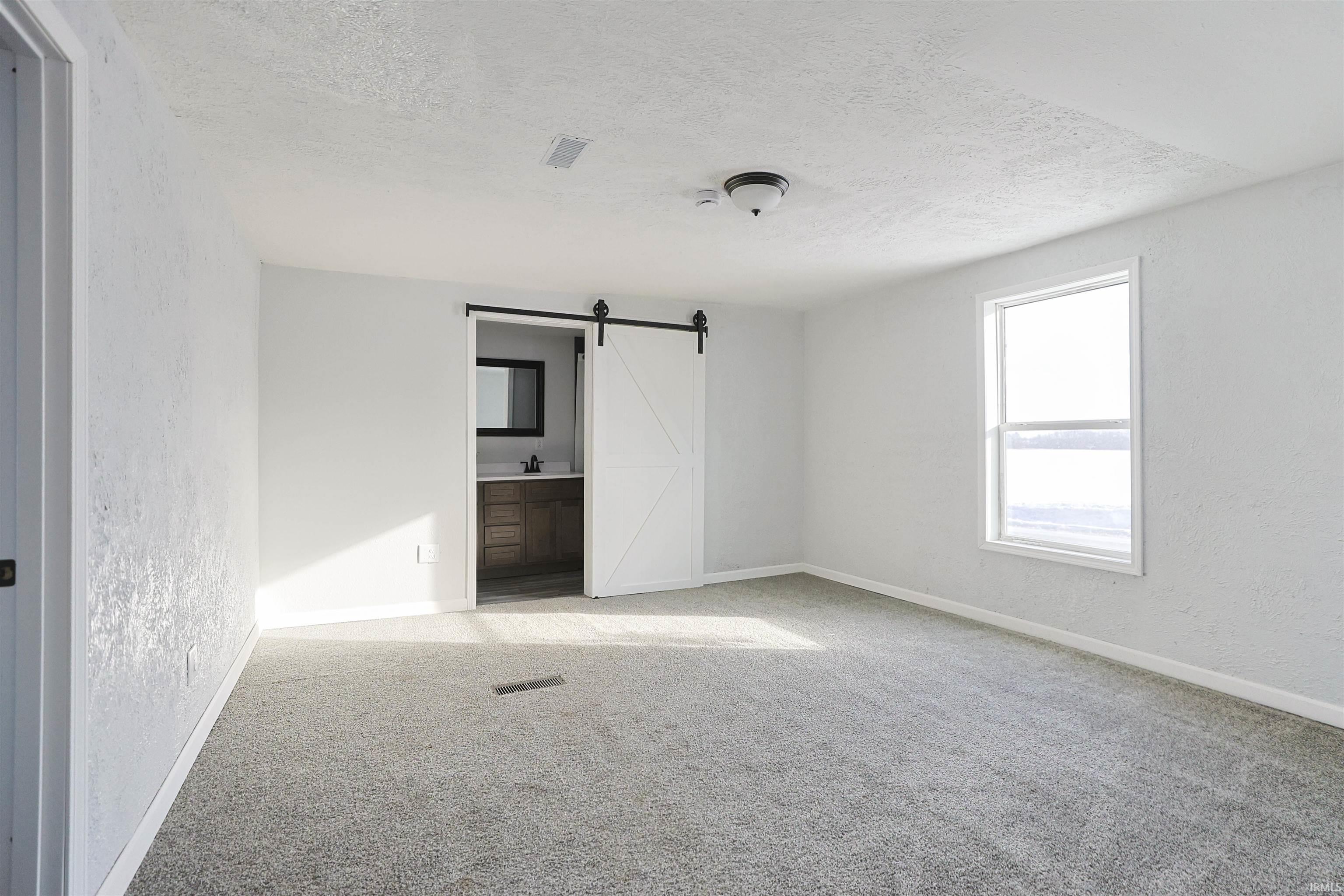 Spare room featuring a barn door, a textured wall, a textured ceiling, and carpet floors