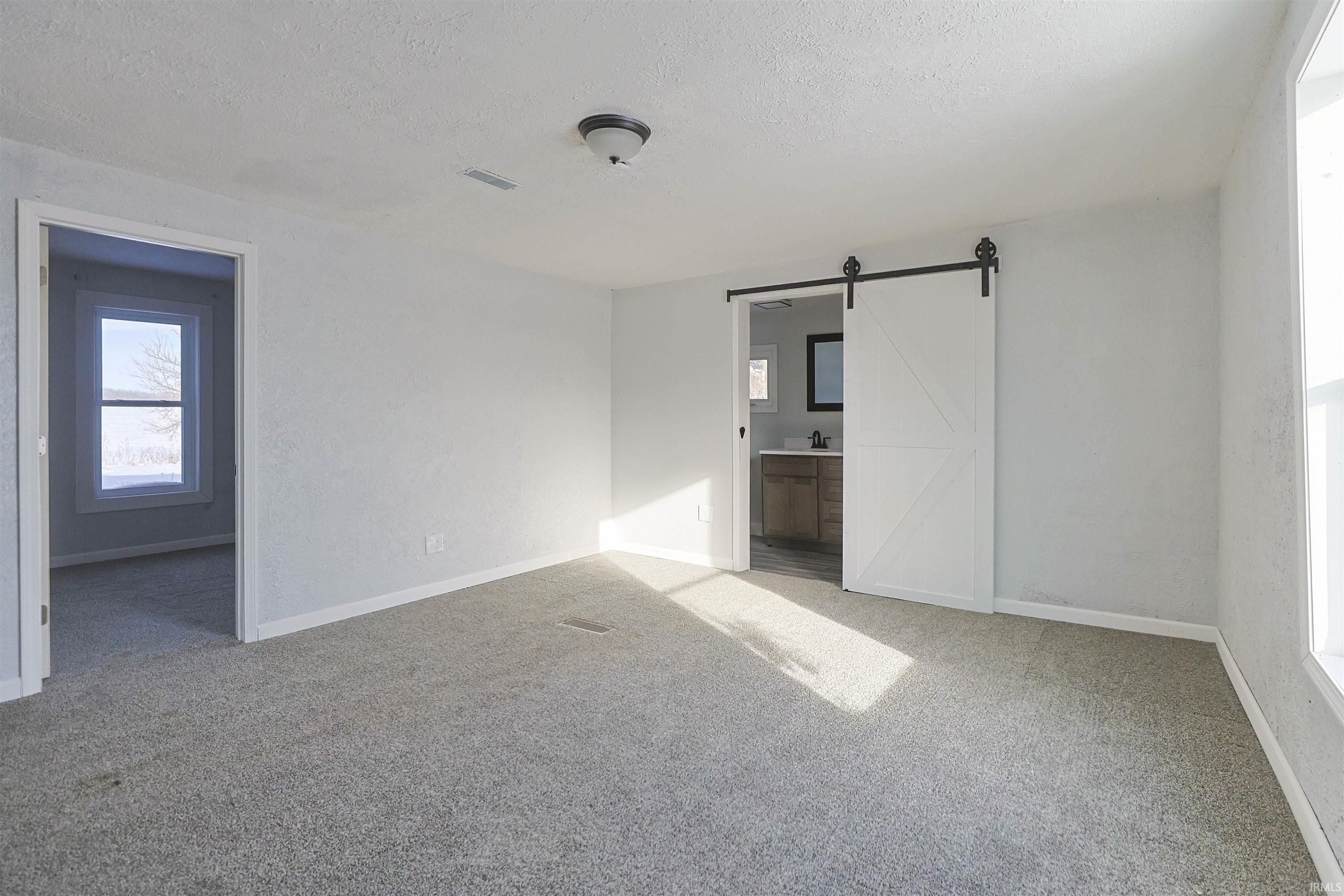 Unfurnished bedroom featuring a barn door, a textured ceiling, light carpet, and ensuite bath