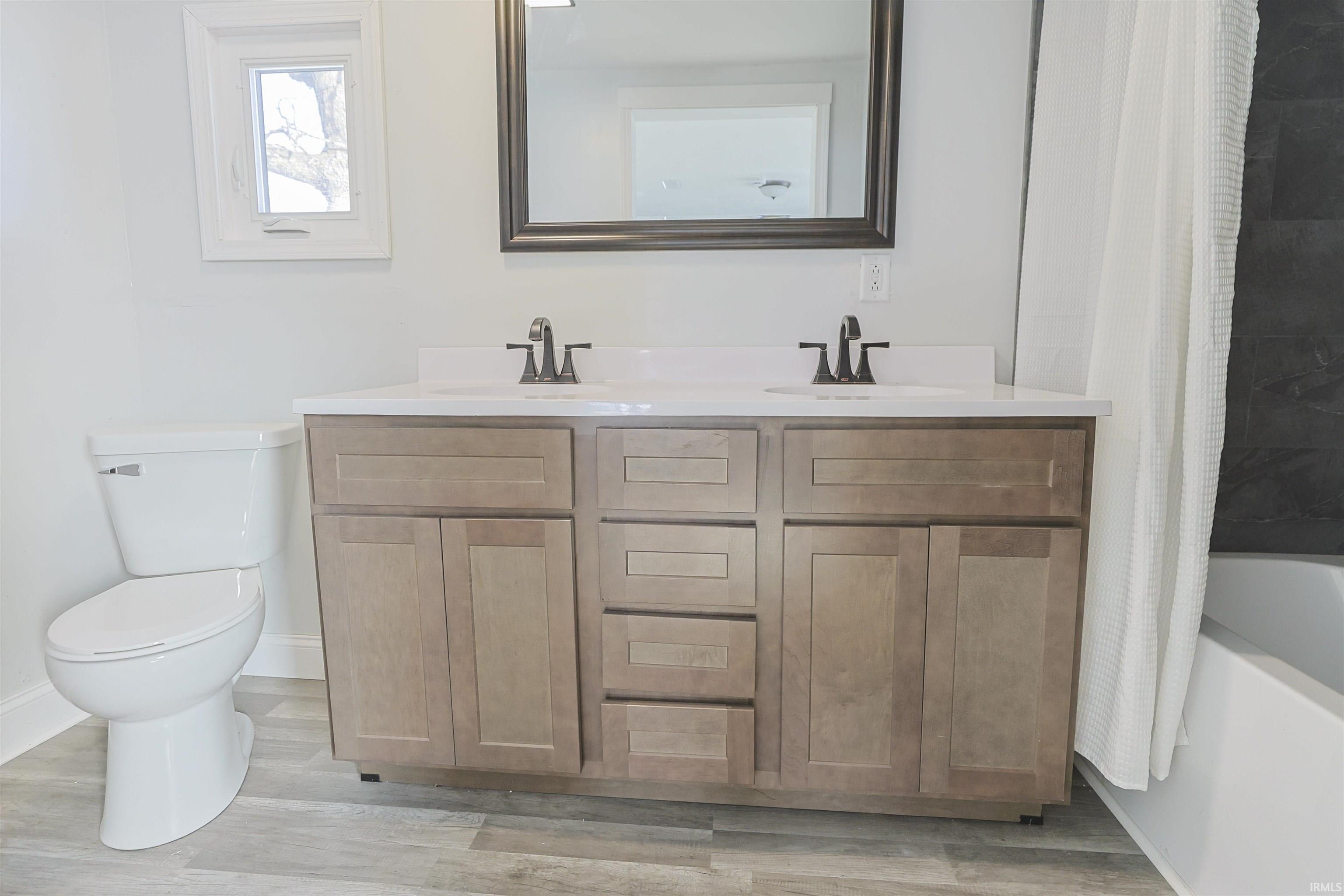 Bathroom with double vanity, shower / bath combo with shower curtain, and light wood finished floors